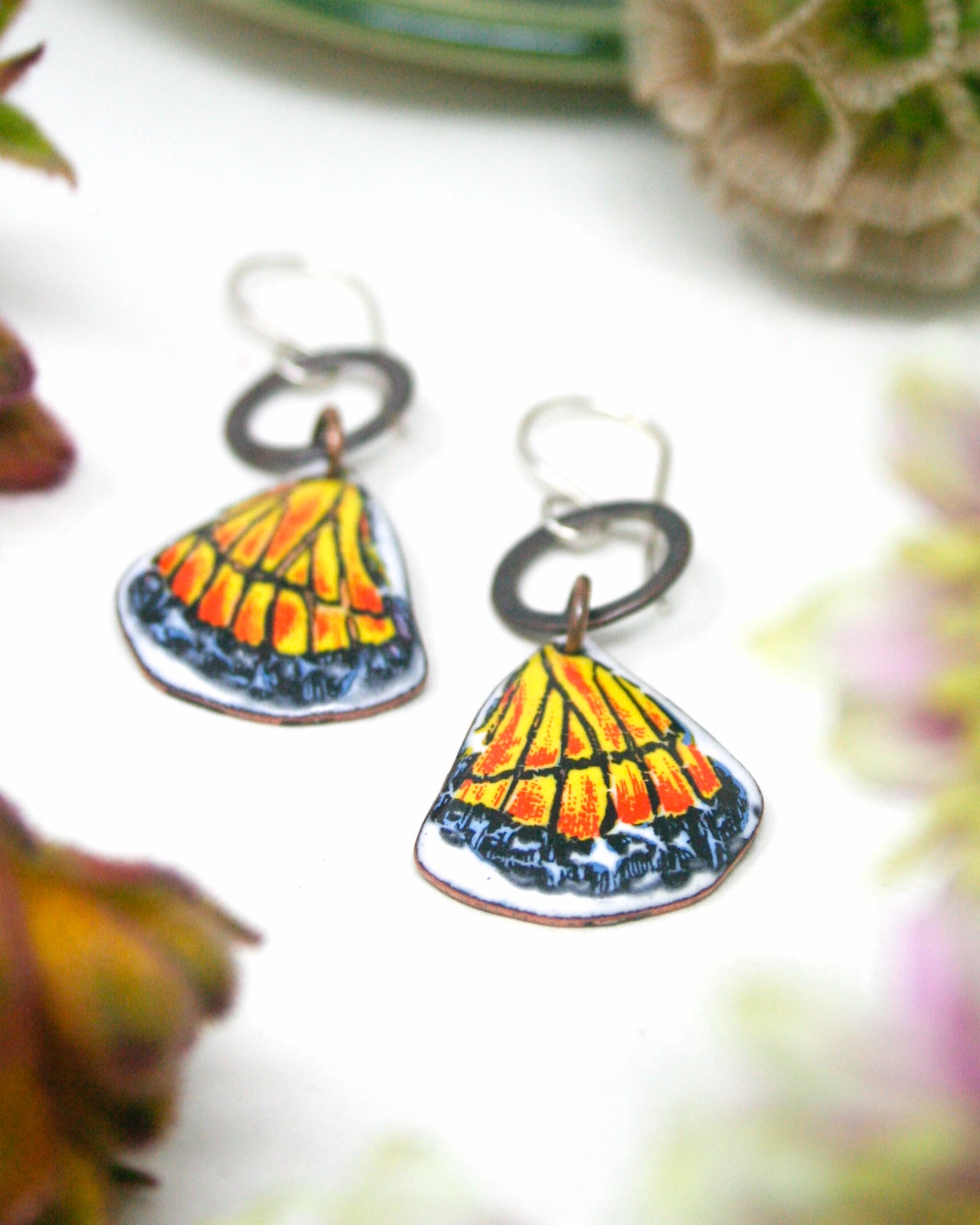 a pair of colorful butterfly-shaped earrings with intricate designs, placed on a white surface.
