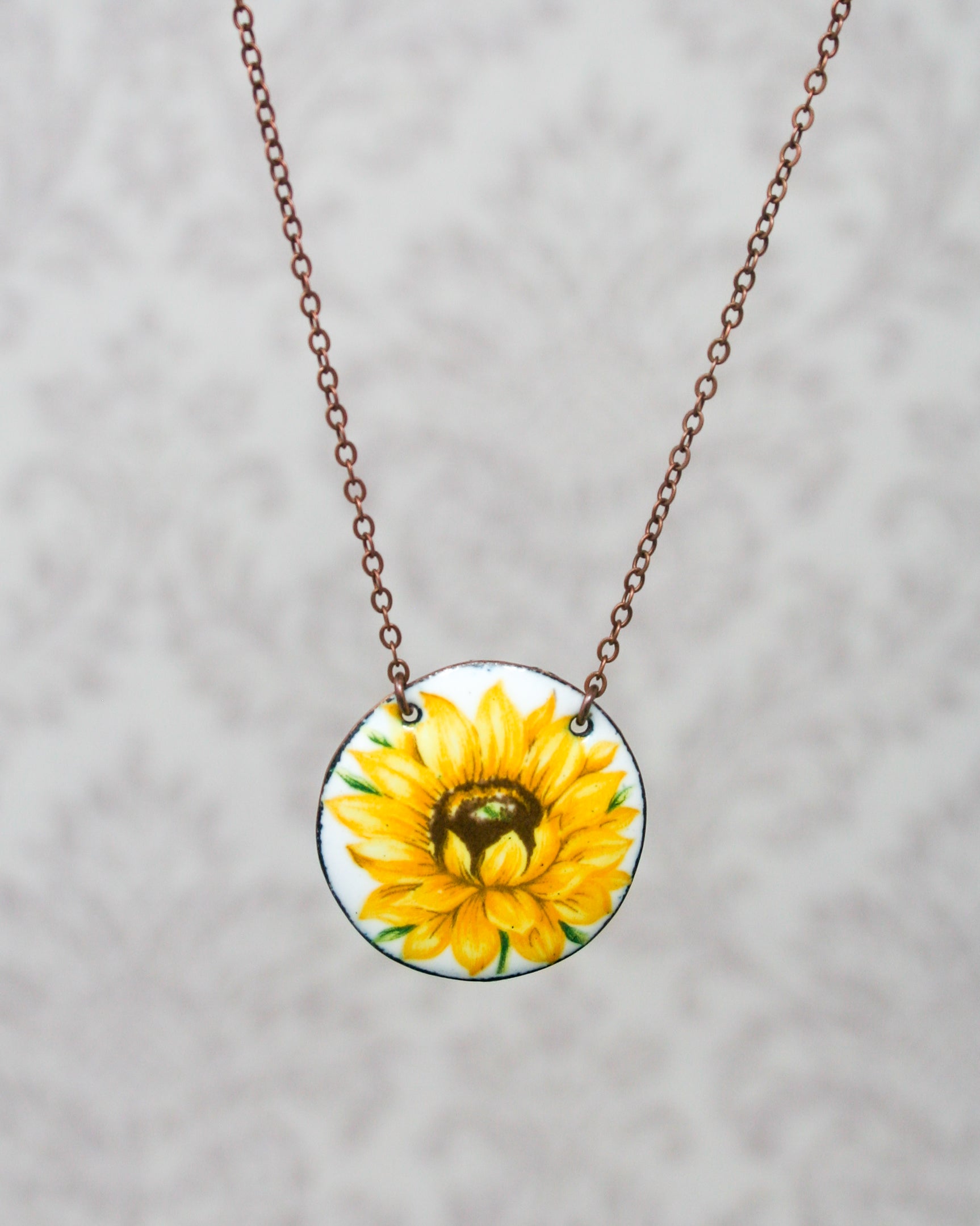 a yellow sunflower painted on a round glass pendant