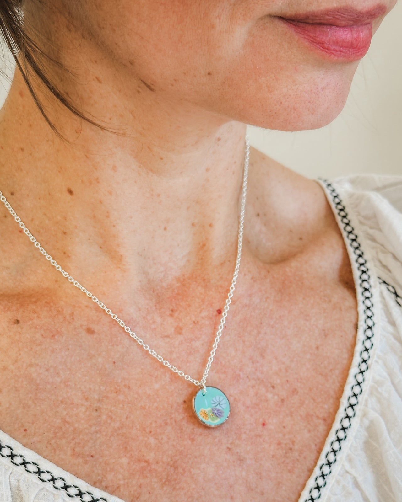 A woman wearing a silver necklace with a blue pendant is shown in the image.