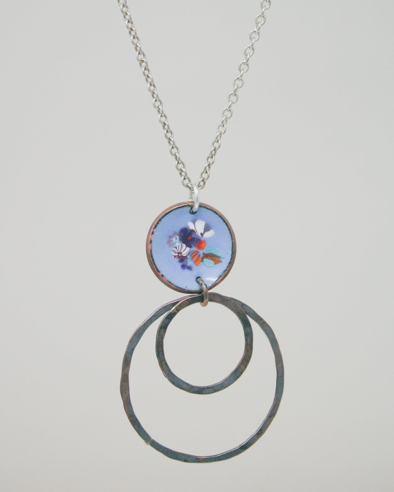 A necklace with a circular pendant featuring a floral design and two metal rings hanging from it.