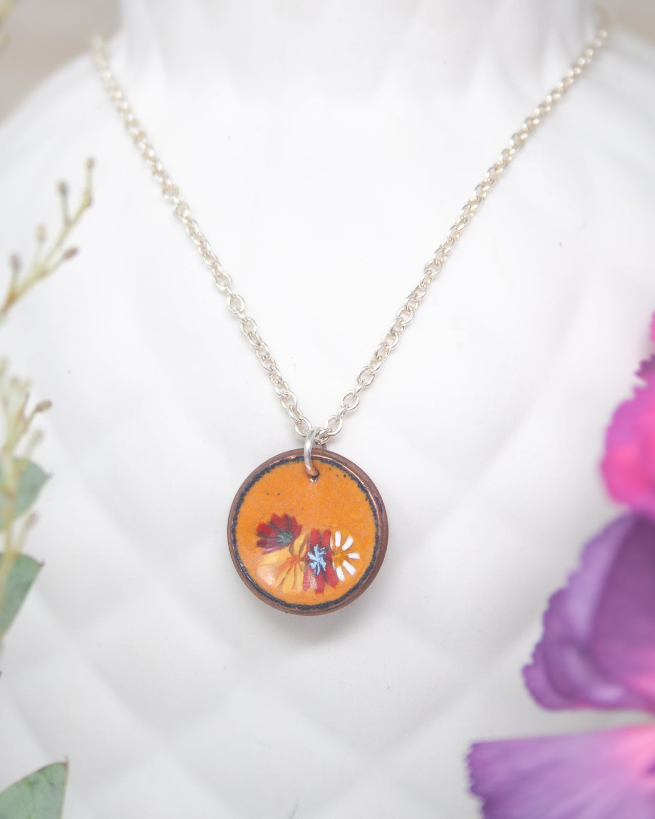 A necklace with a circular pendant featuring a floral design in orange and purple colors.