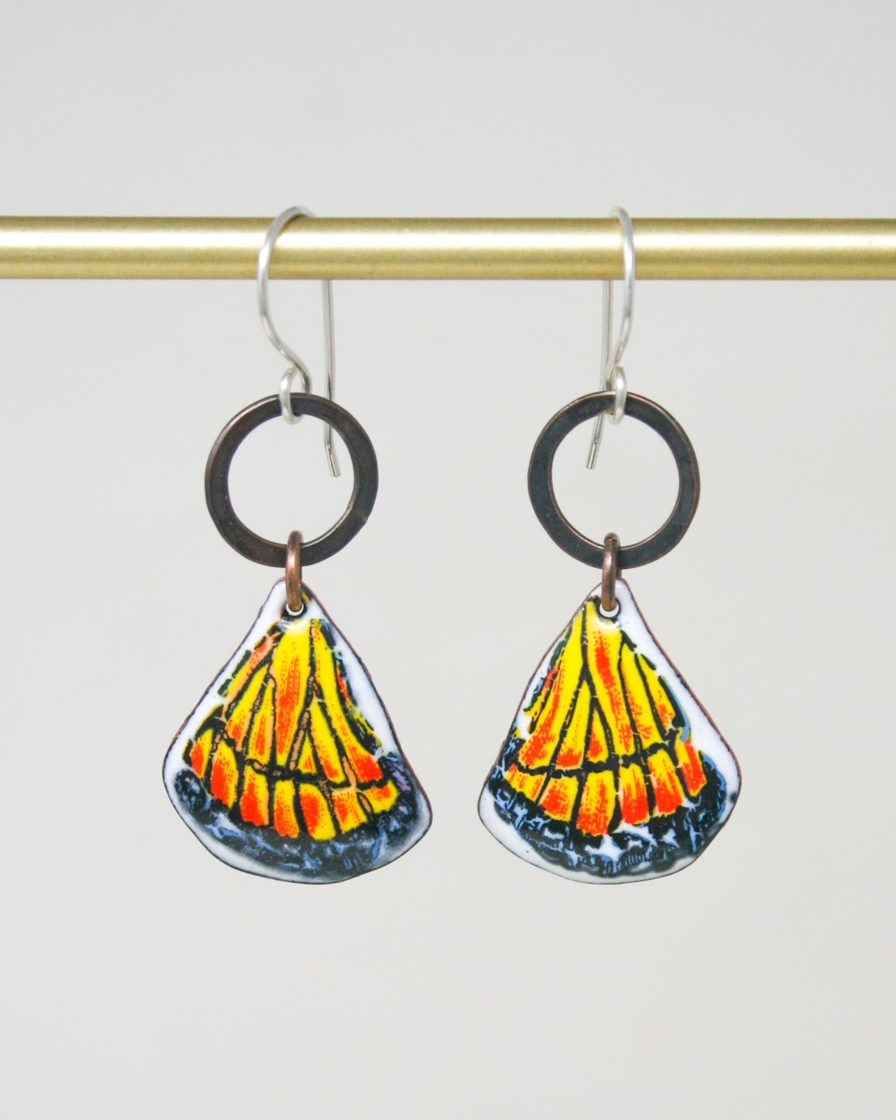 A pair of earrings with a design of a yellow and orange shell or flower-like shape hanging from a hook.