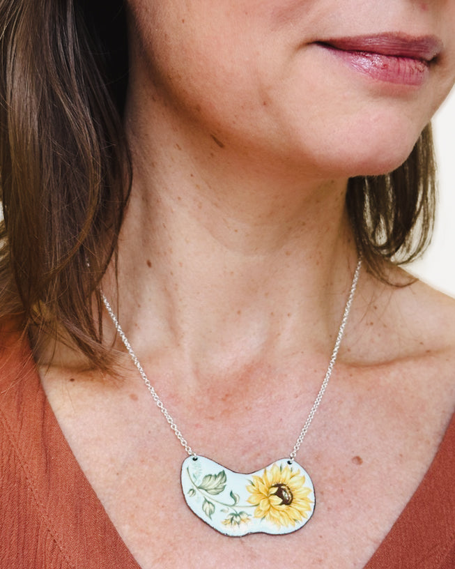 a woman wearing a necklace with a sunflower on it