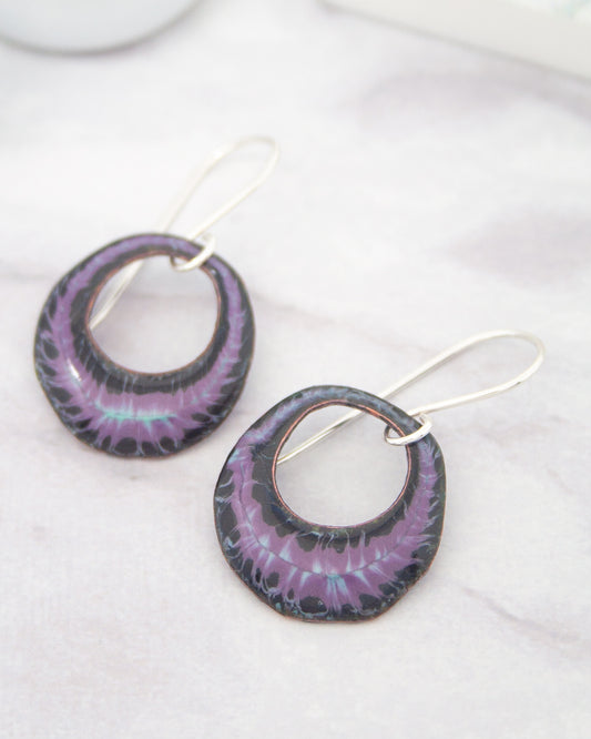 A pair of earrings with purple and black metallic designs, featuring circular cutouts and a metallic chain.