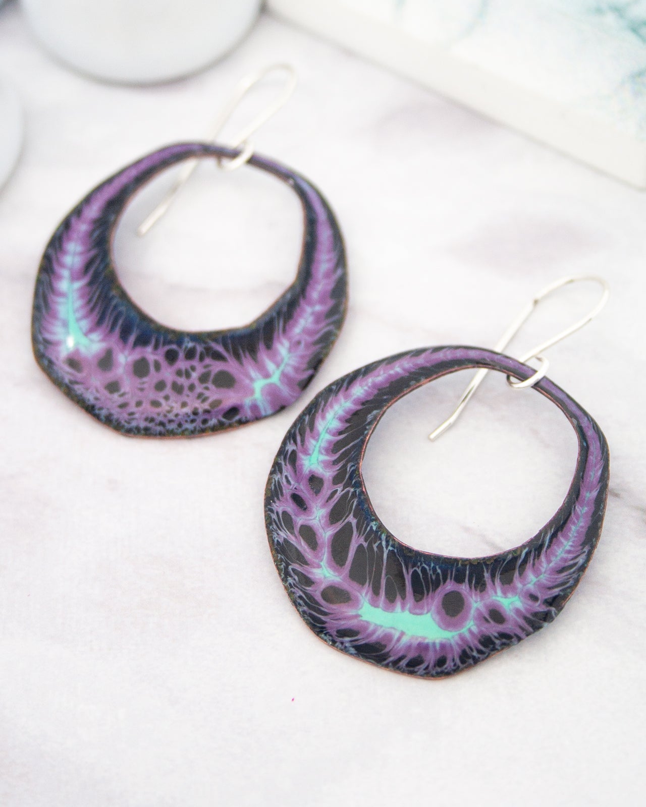 A pair of purple and black earrings with a unique, abstract design featuring a swirling pattern of purple and black lines.