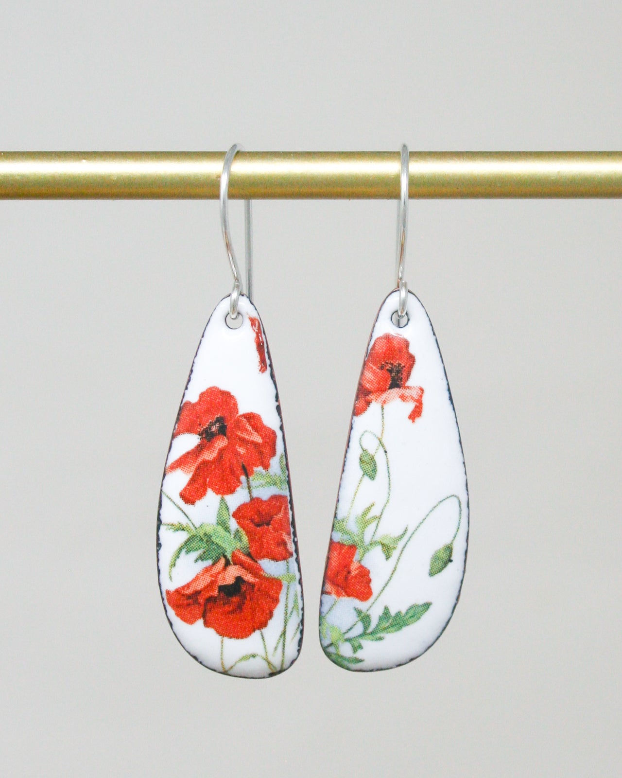 A pair of earrings with red flowers on a white background, hanging from a gold bar.
