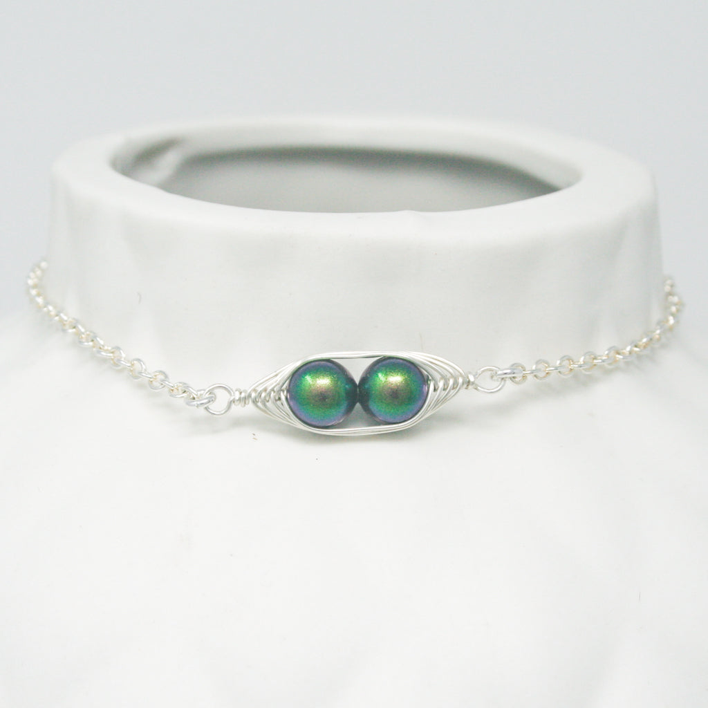 a white necklace with two green beads on it