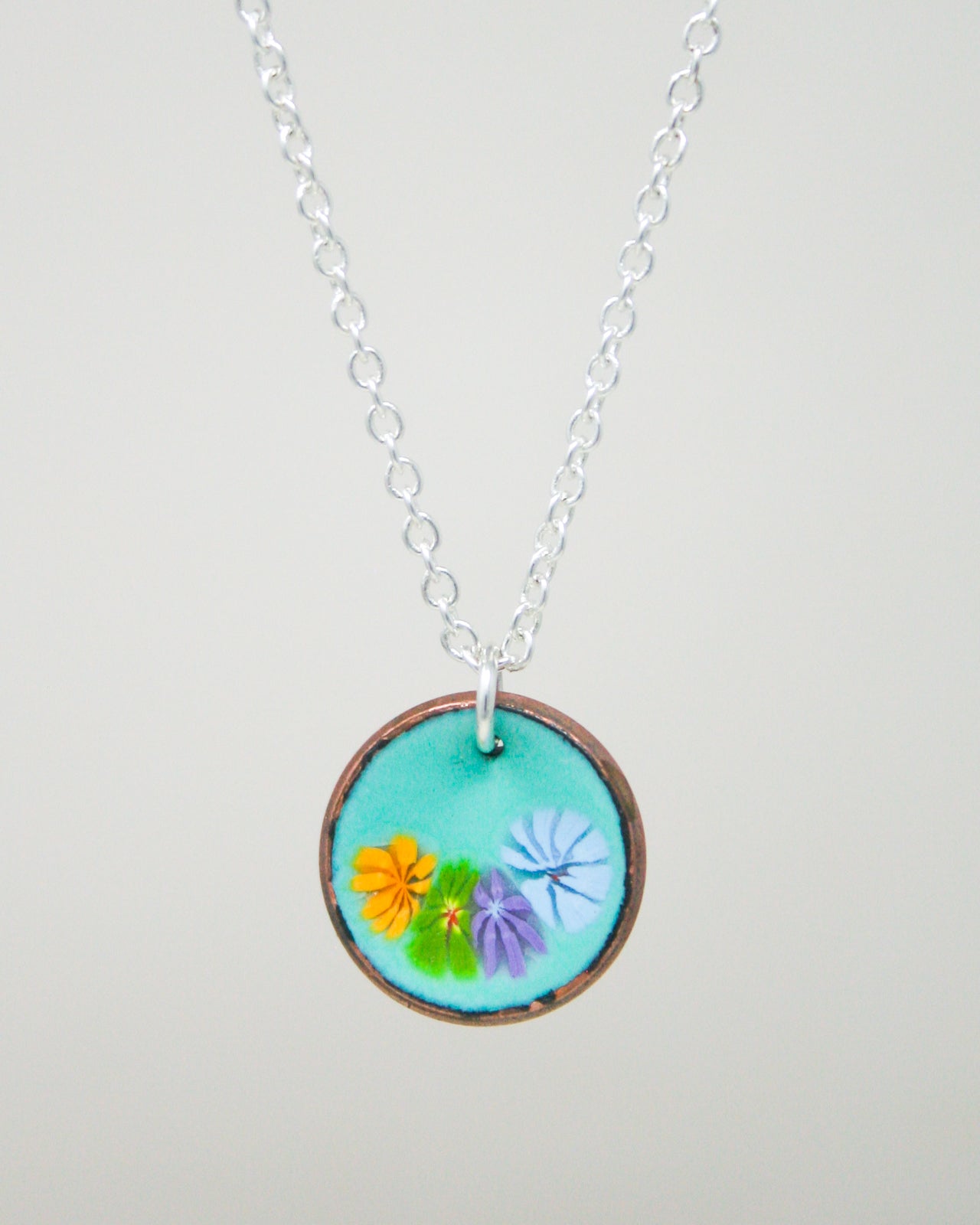 A necklace with a circular pendant featuring a vibrant floral design in various colors.