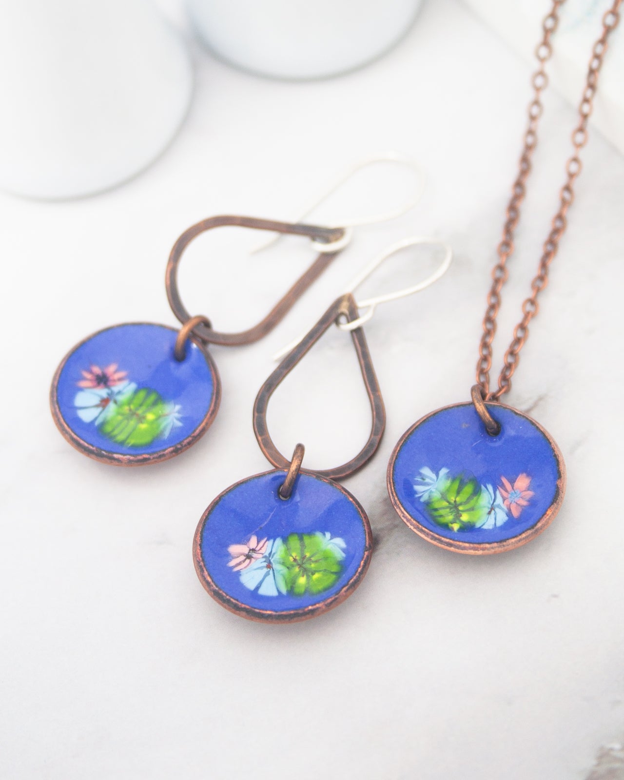 a pair of blue earrings and a necklace with blue and green floral designs.