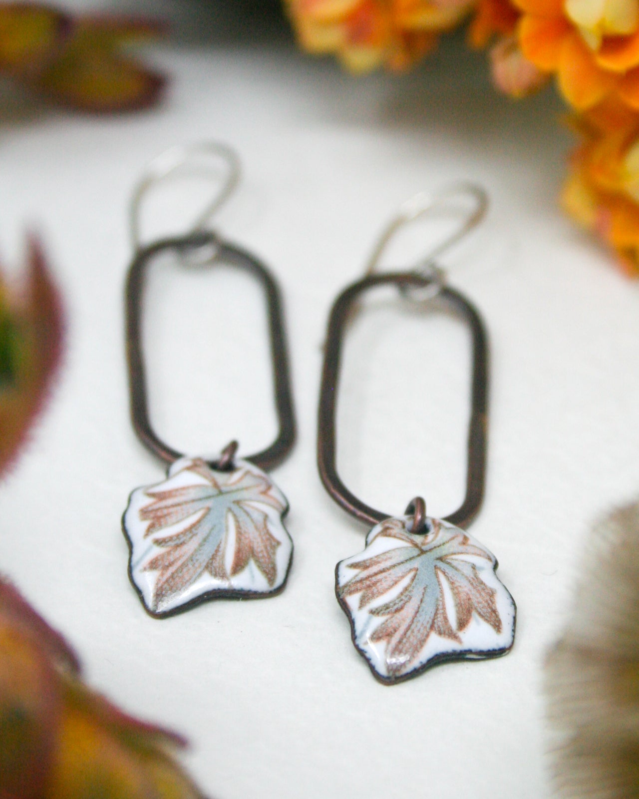 A pair of earrings with leaf-shaped pendants, featuring a combination of blue and green colors, are displayed on a white surface.