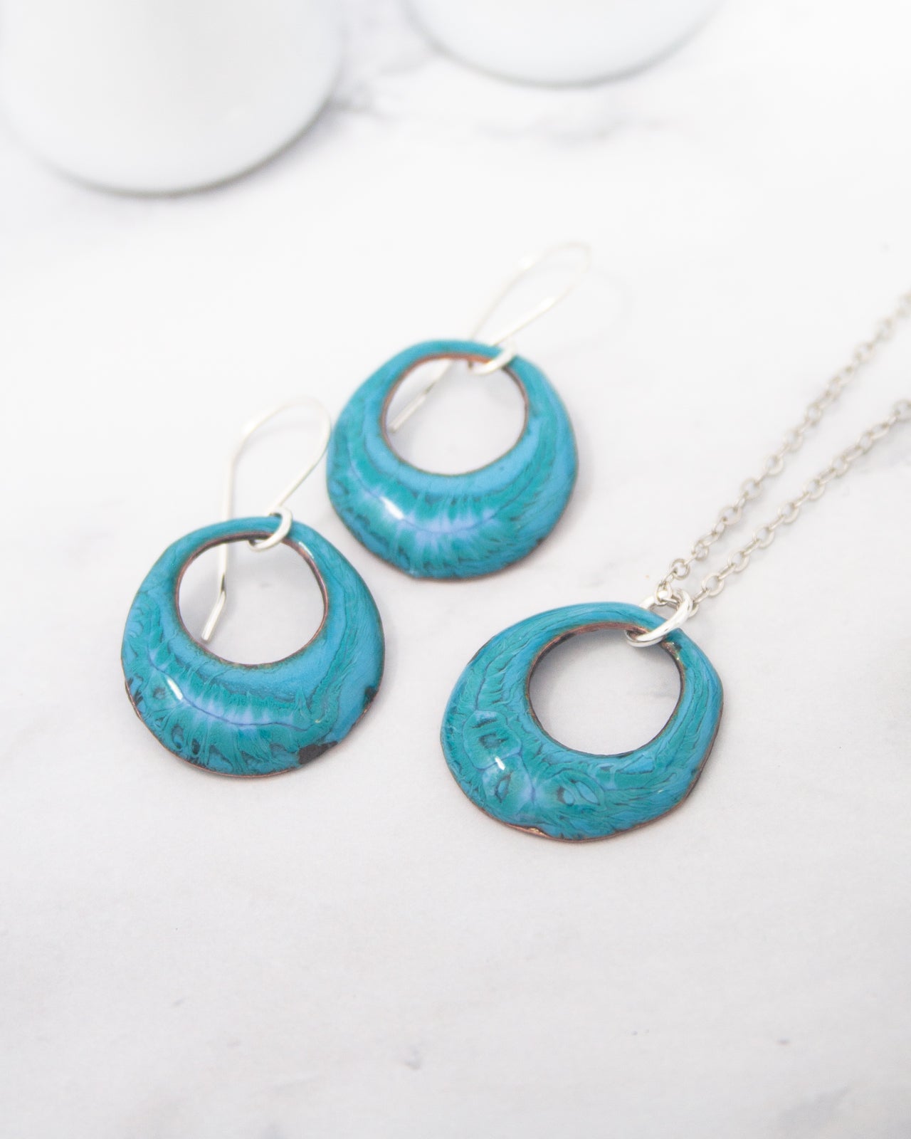A pair of turquoise-colored earrings and a necklace with turquoise-colored pendants are displayed on a white marble surface.