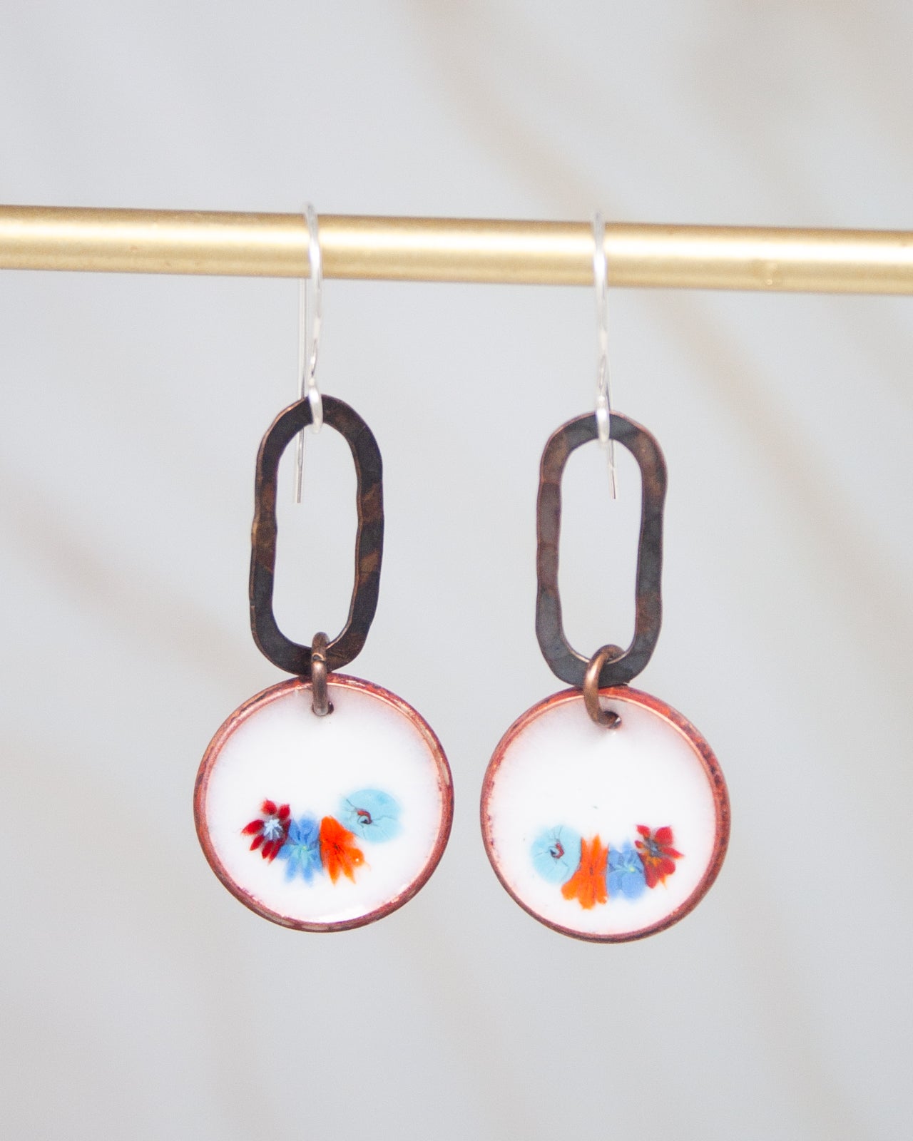 A pair of earrings with a floral design on the circular pendants, hanging from a gold-colored metal hook.