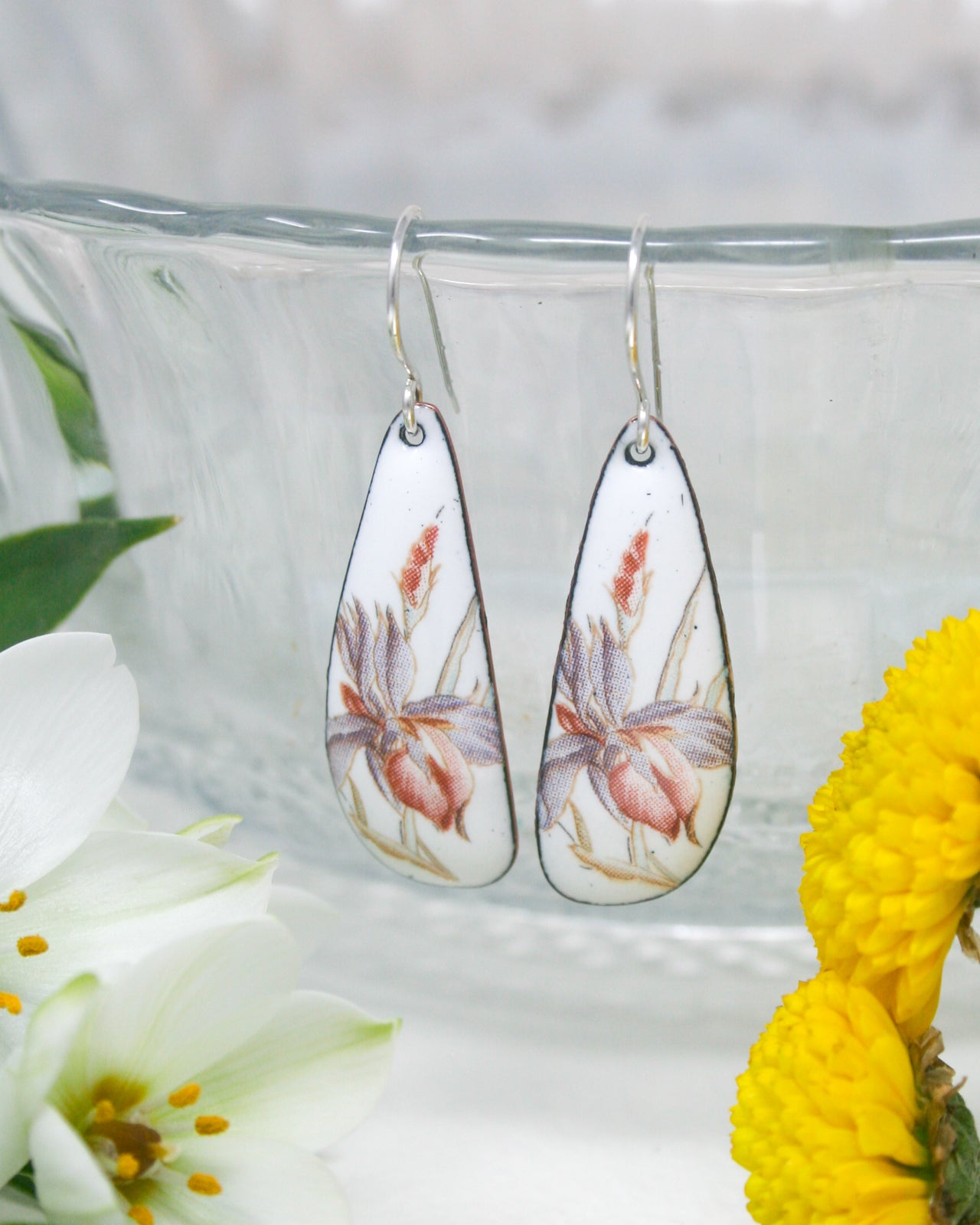 a close up of a pair of earrings with flowers in the background