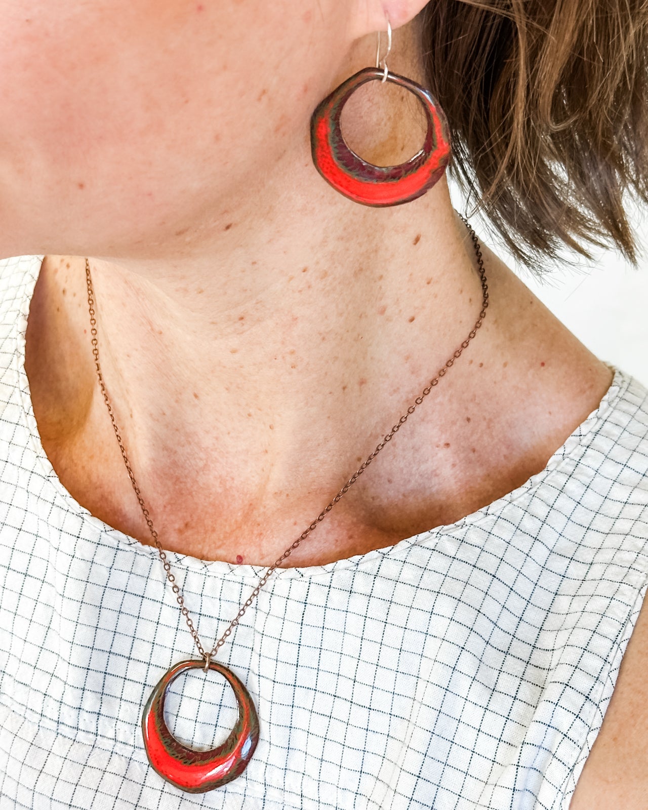 A woman wearing a necklace with a red pendant and matching red earrings.