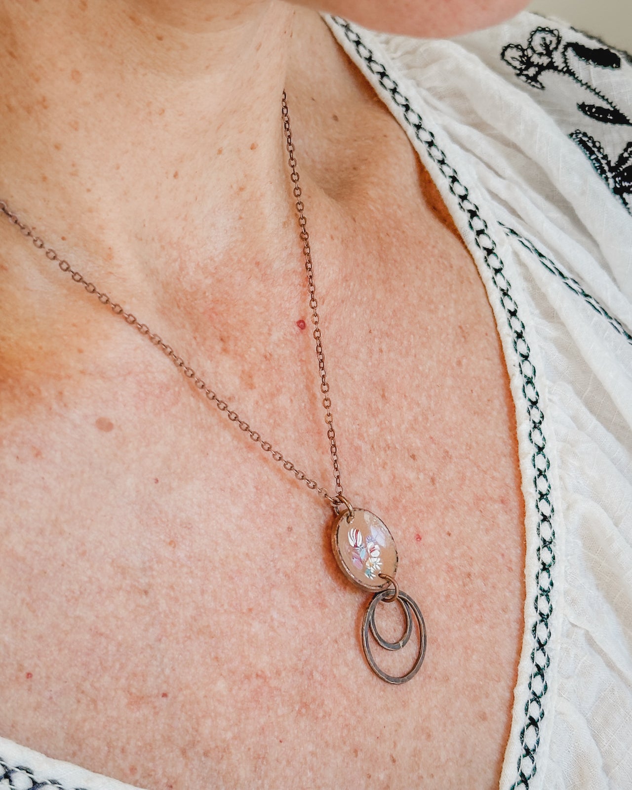 A close-up view of a woman's neck and chest area, showing a delicate necklace with a pendant.
