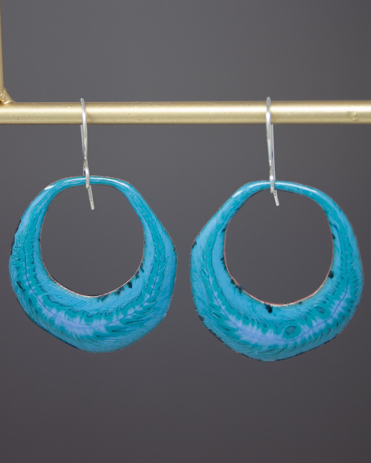 A pair of turquoise-colored hoop earrings hanging from a gold-colored metal hook.
