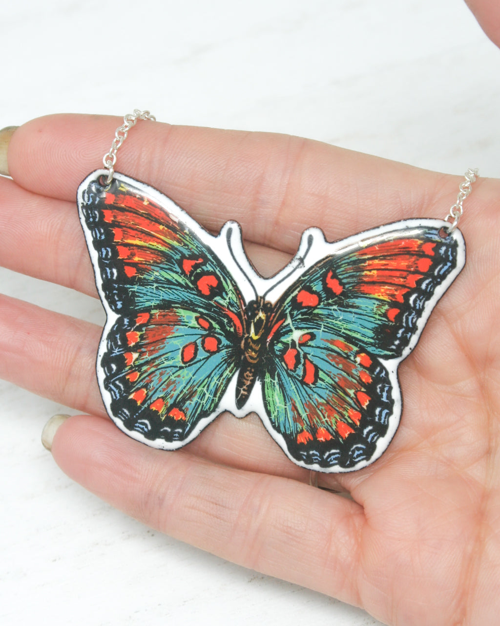 a hand holding a butterfly shaped pendant on a chain