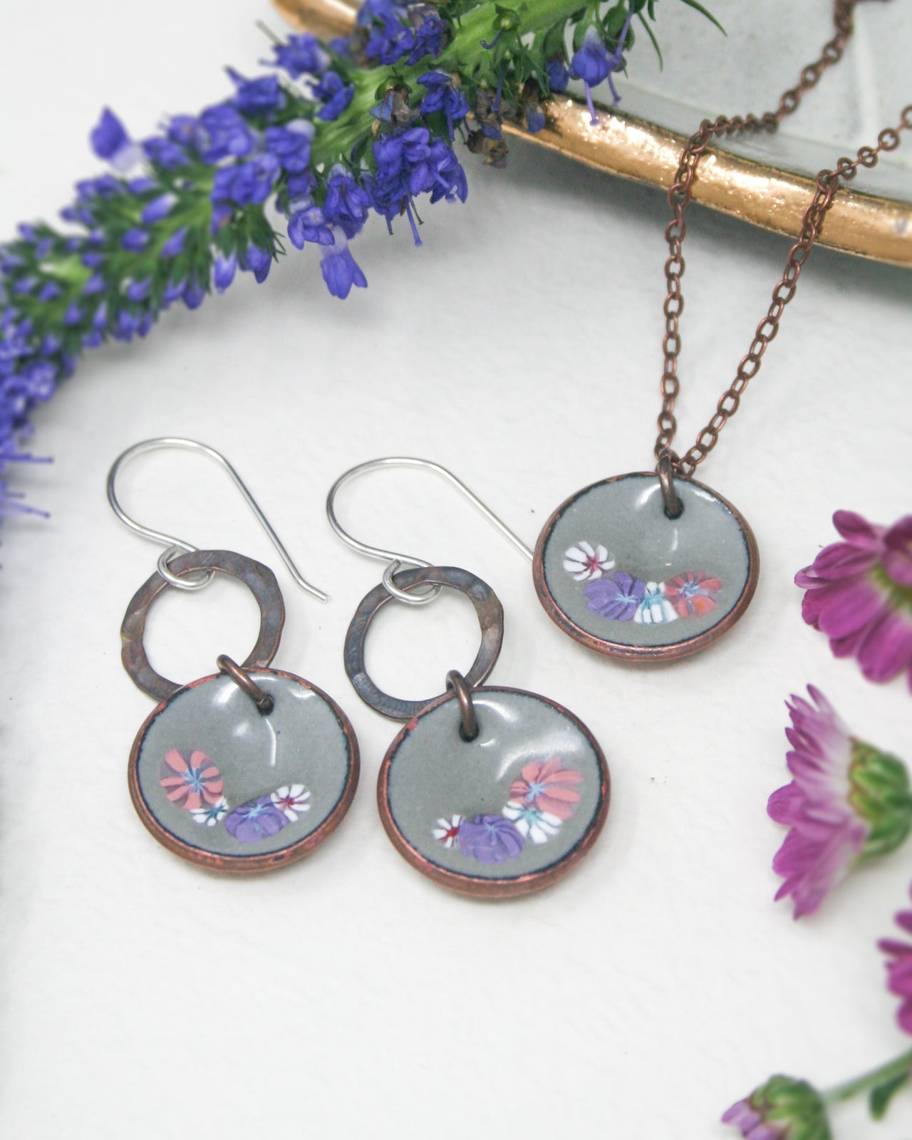 three pieces of jewelry sitting next to purple flowers