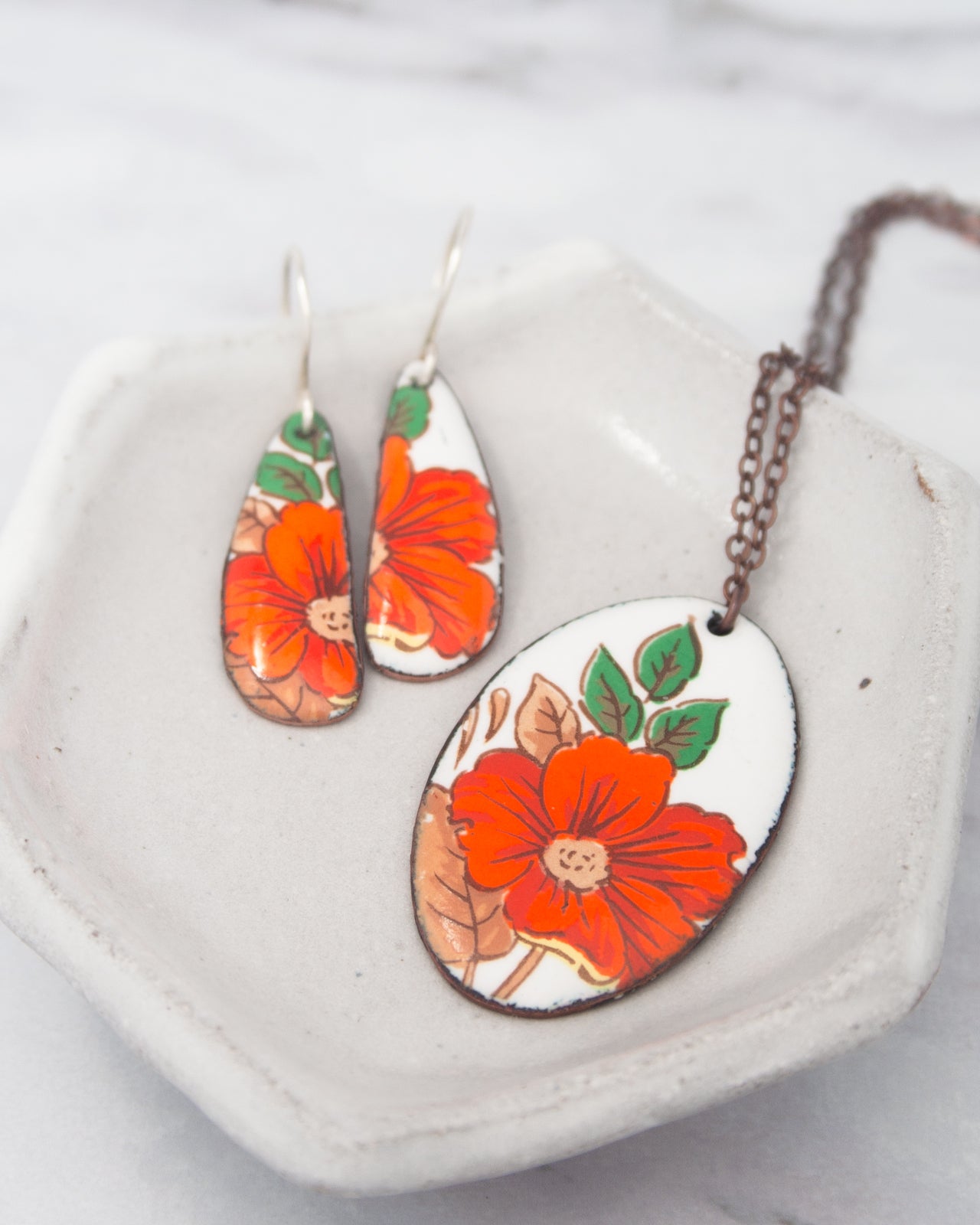 A pair of earrings and a necklace with floral designs are displayed on a white surface.