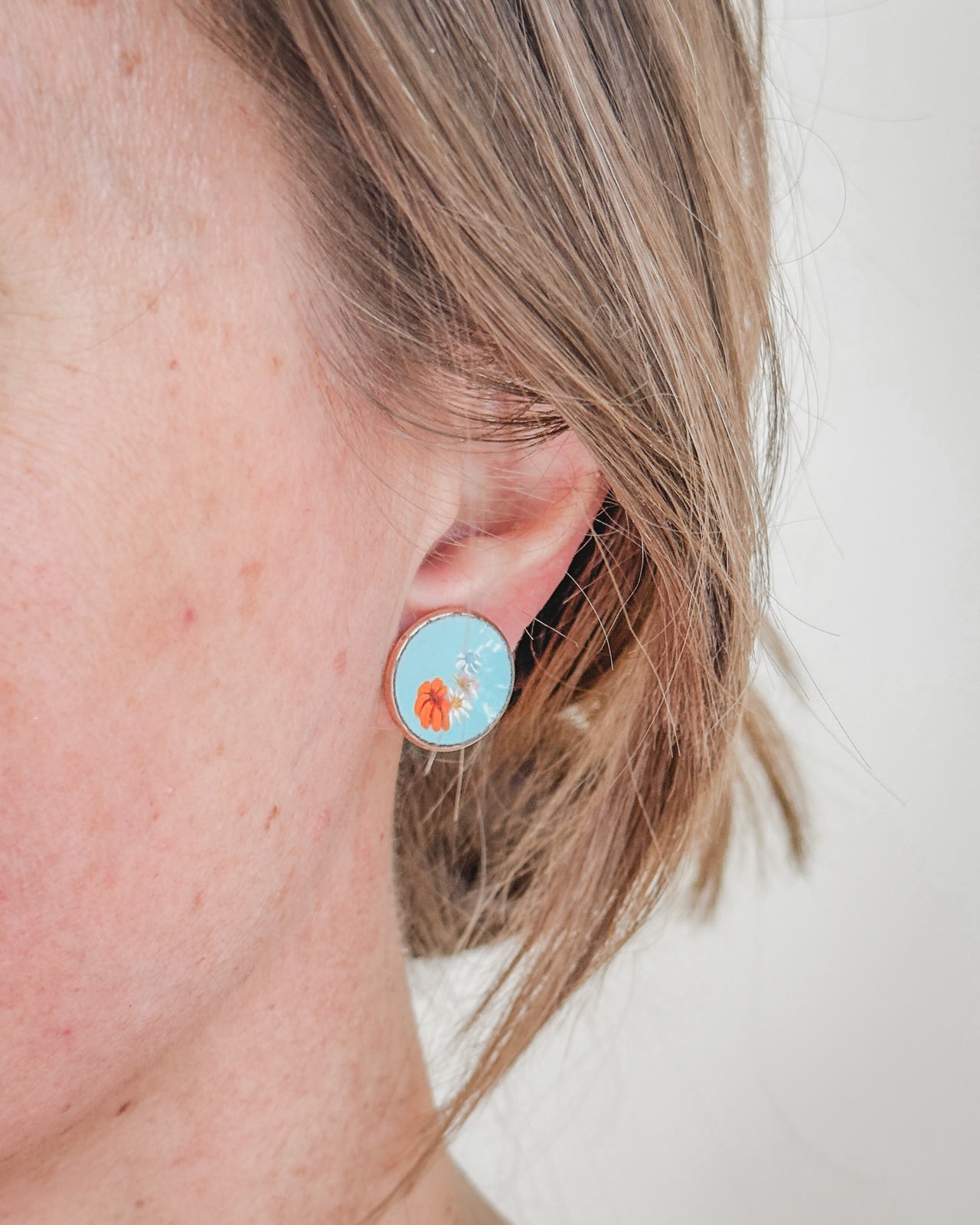 A close-up view of a person's ear wearing a blue circular earring with a floral design.