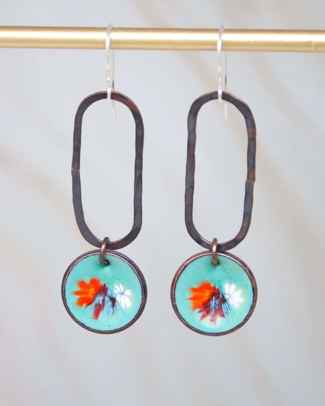 A pair of earrings with a floral design on the center, hanging from a gold-colored metal hook.