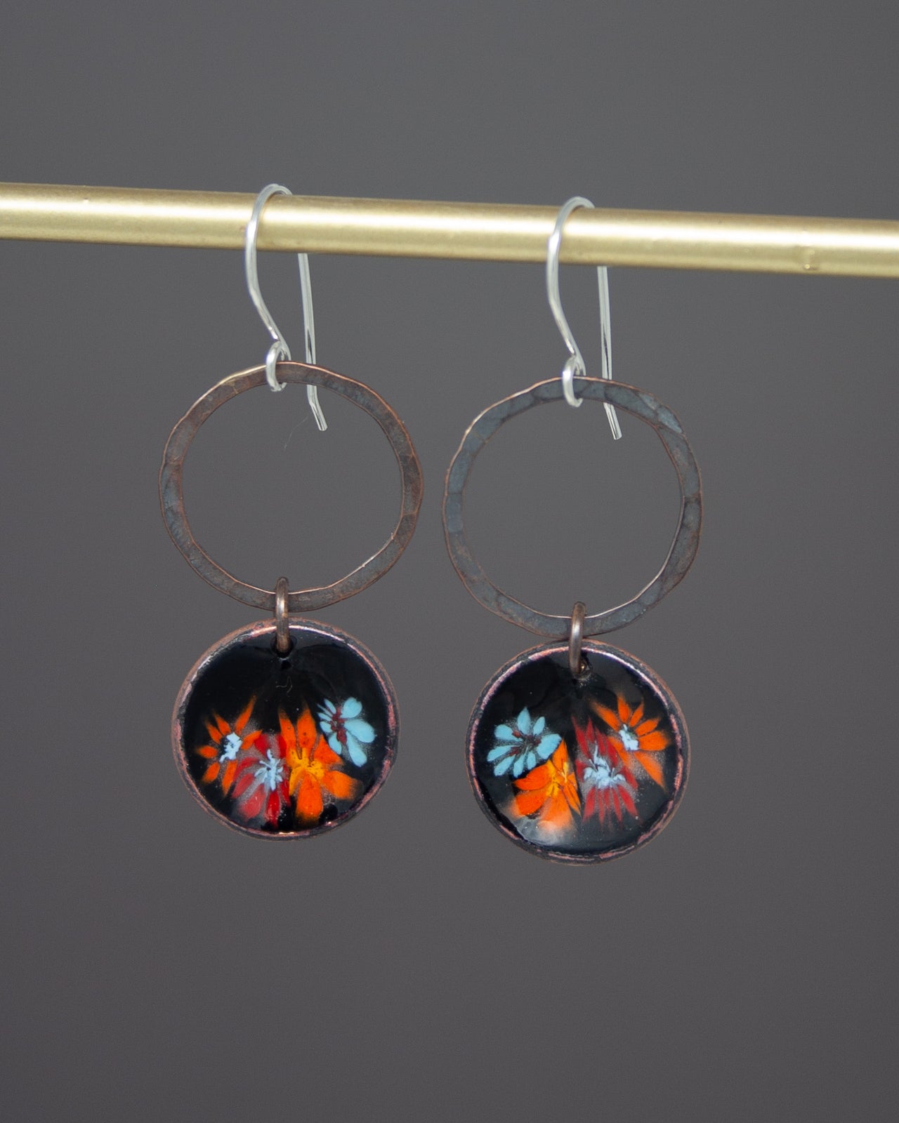 A pair of earrings with circular designs featuring colorful flowers hanging from a metal hook.