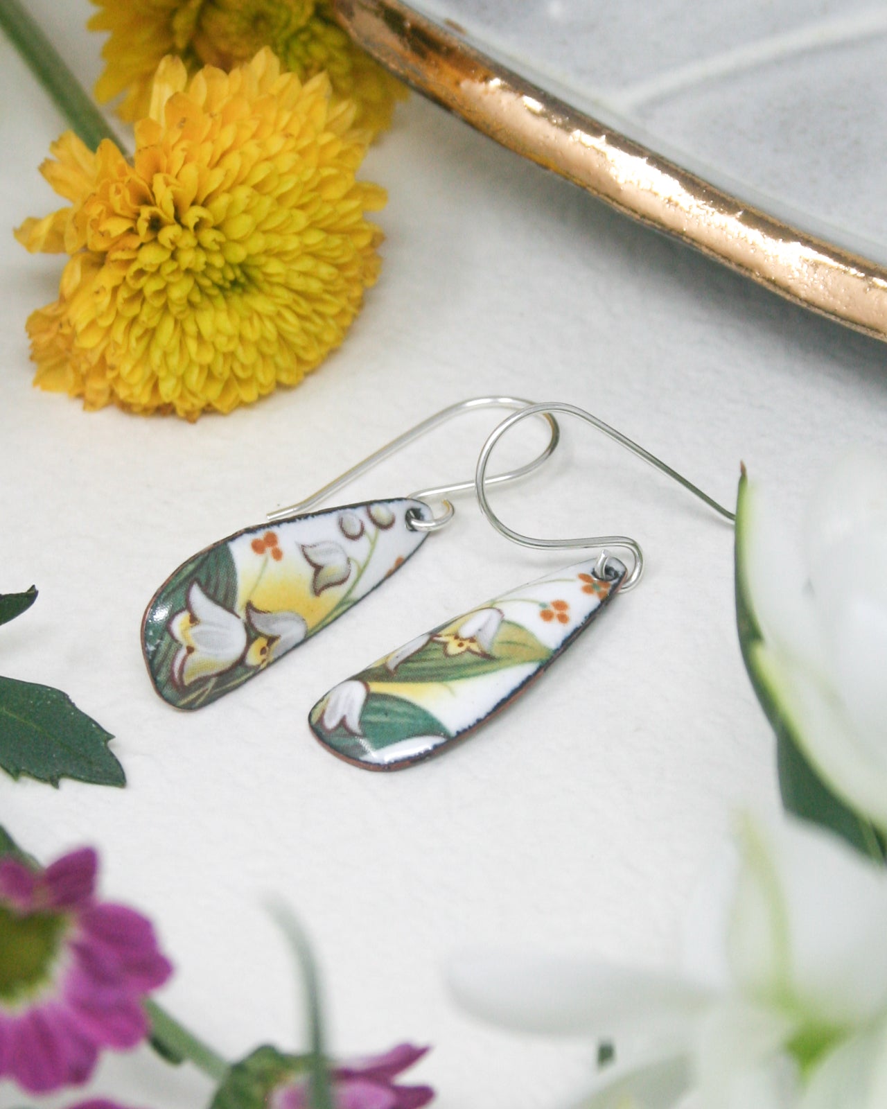 a pair of earrings sitting on top of a table next to flowers