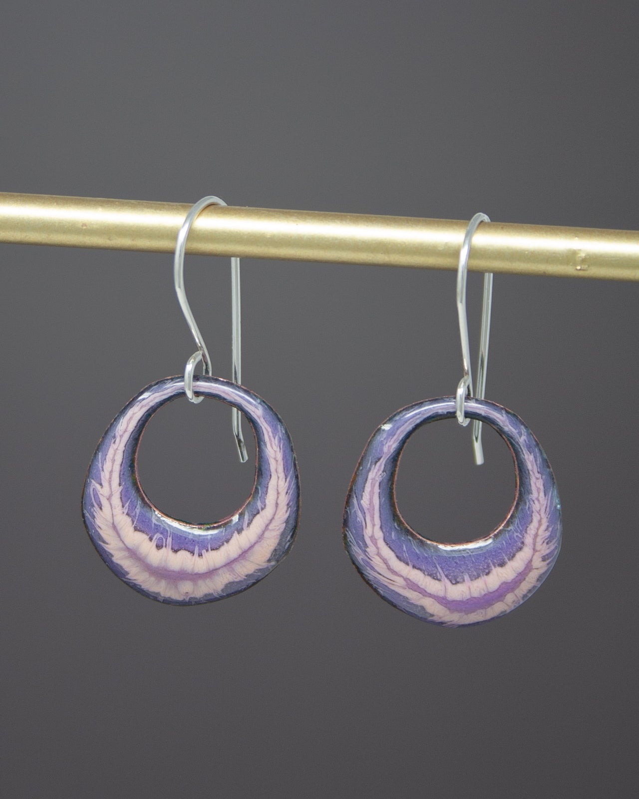 A pair of earrings with purple and pink swirl designs hanging from a gold bar.