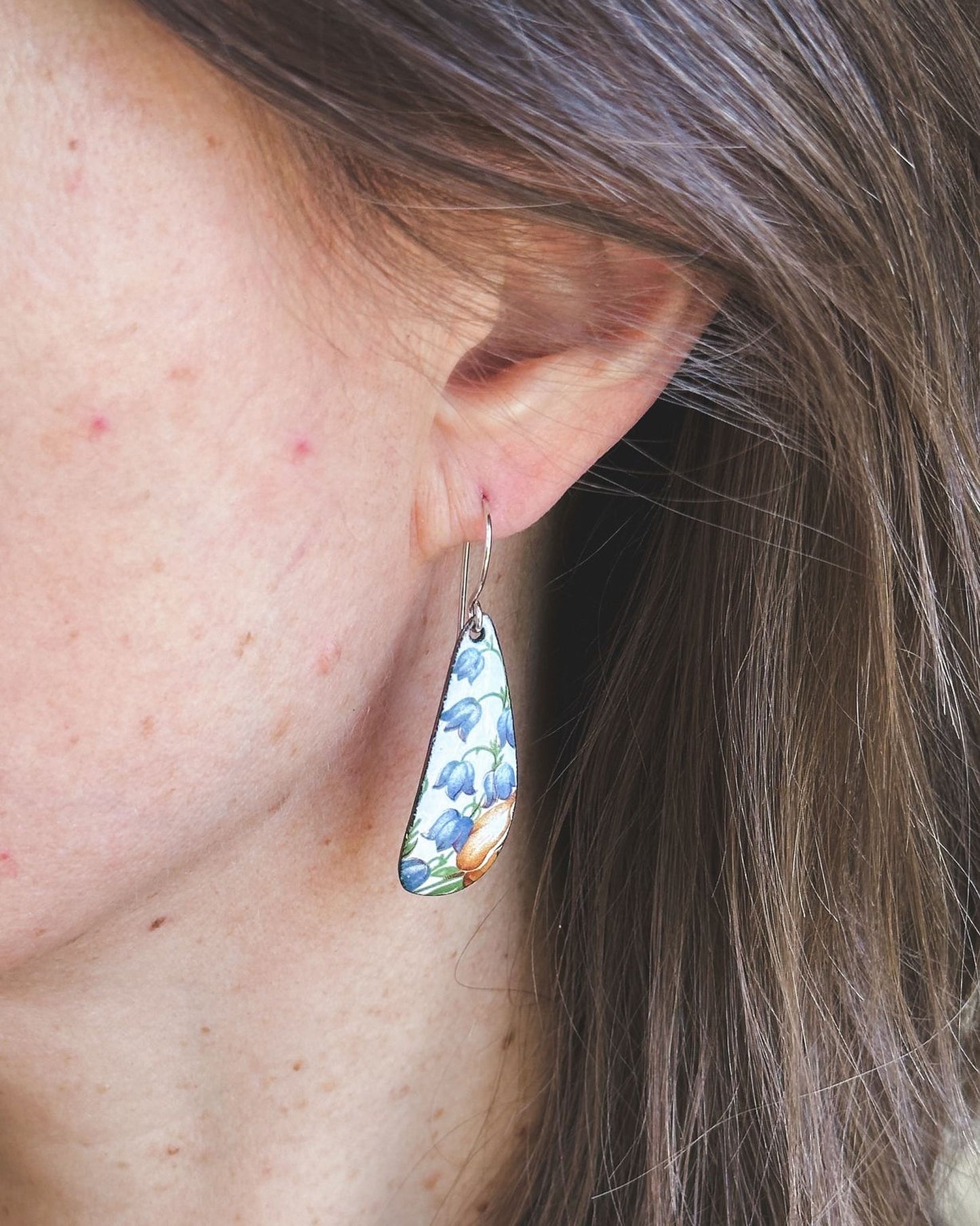 A close-up view of a person's ear wearing a pair of earrings with a floral pattern.