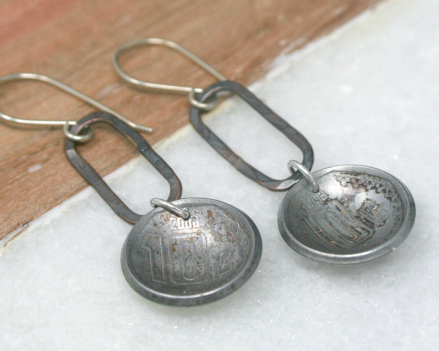 a pair of silver earrings sitting on top of a piece of wood