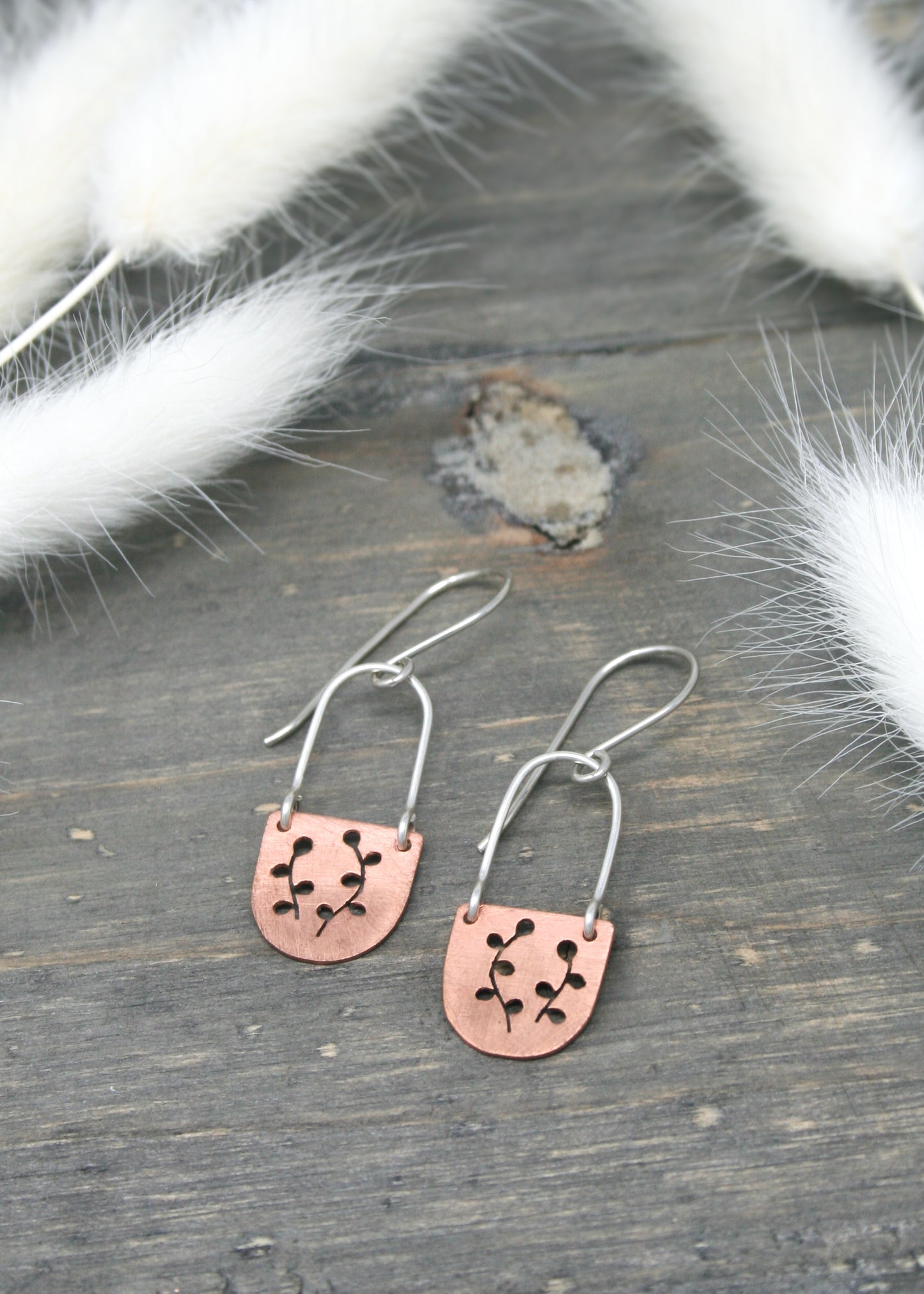 a pair of pink and silver earrings on a wooden surface