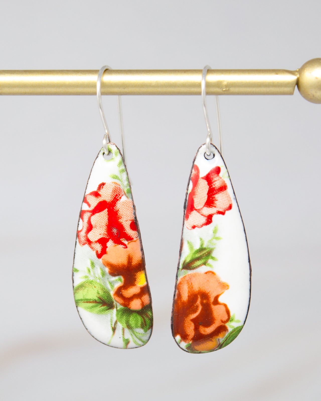 A pair of earrings with a floral design, featuring red and orange flowers on a white background.
