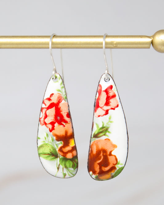 A pair of earrings with a floral design, featuring red and orange flowers on a white background.