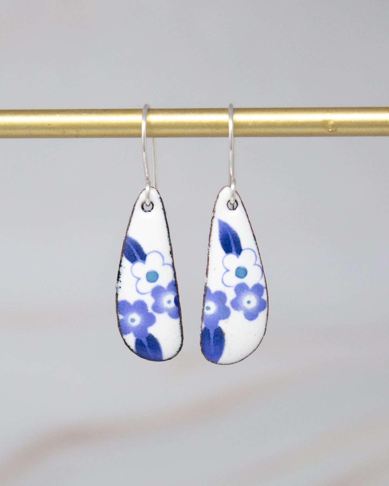 A pair of earrings with blue and white floral designs hanging from a gold bar.