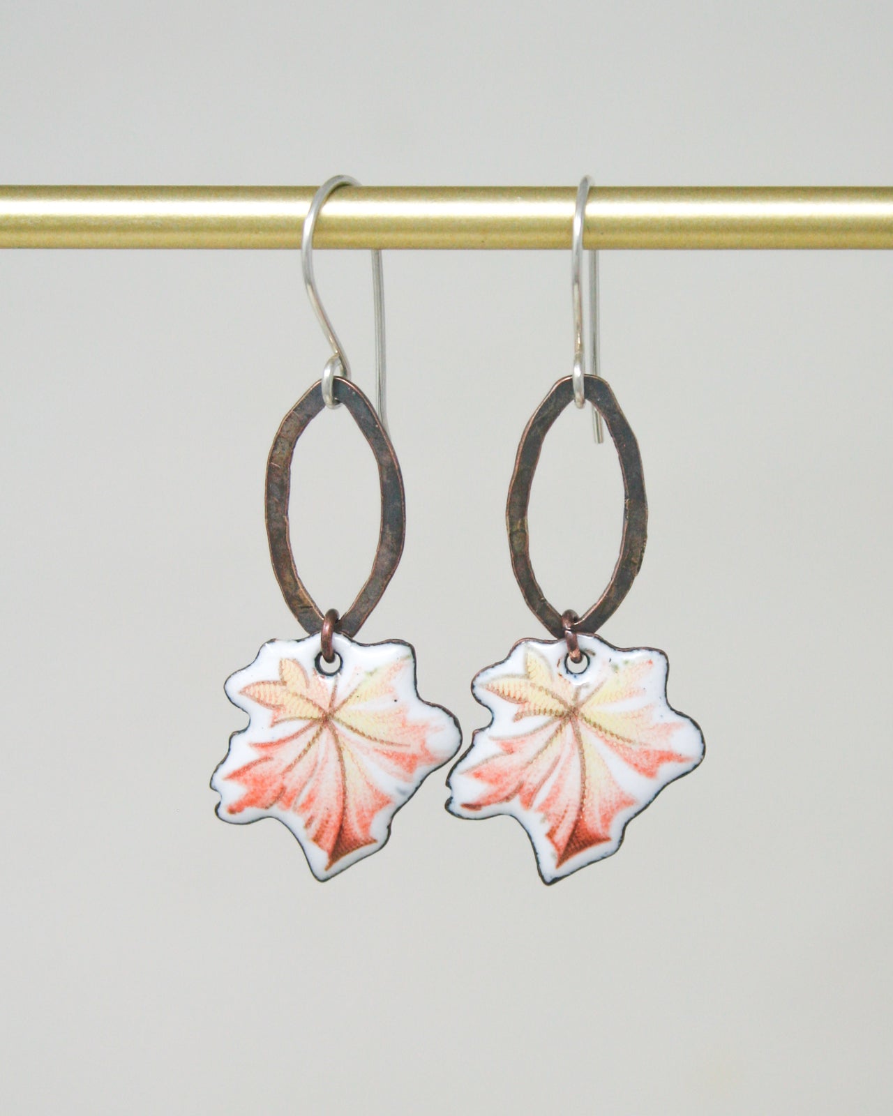 A pair of earrings with leaf-shaped pendants hanging from a gold-colored metal hook.