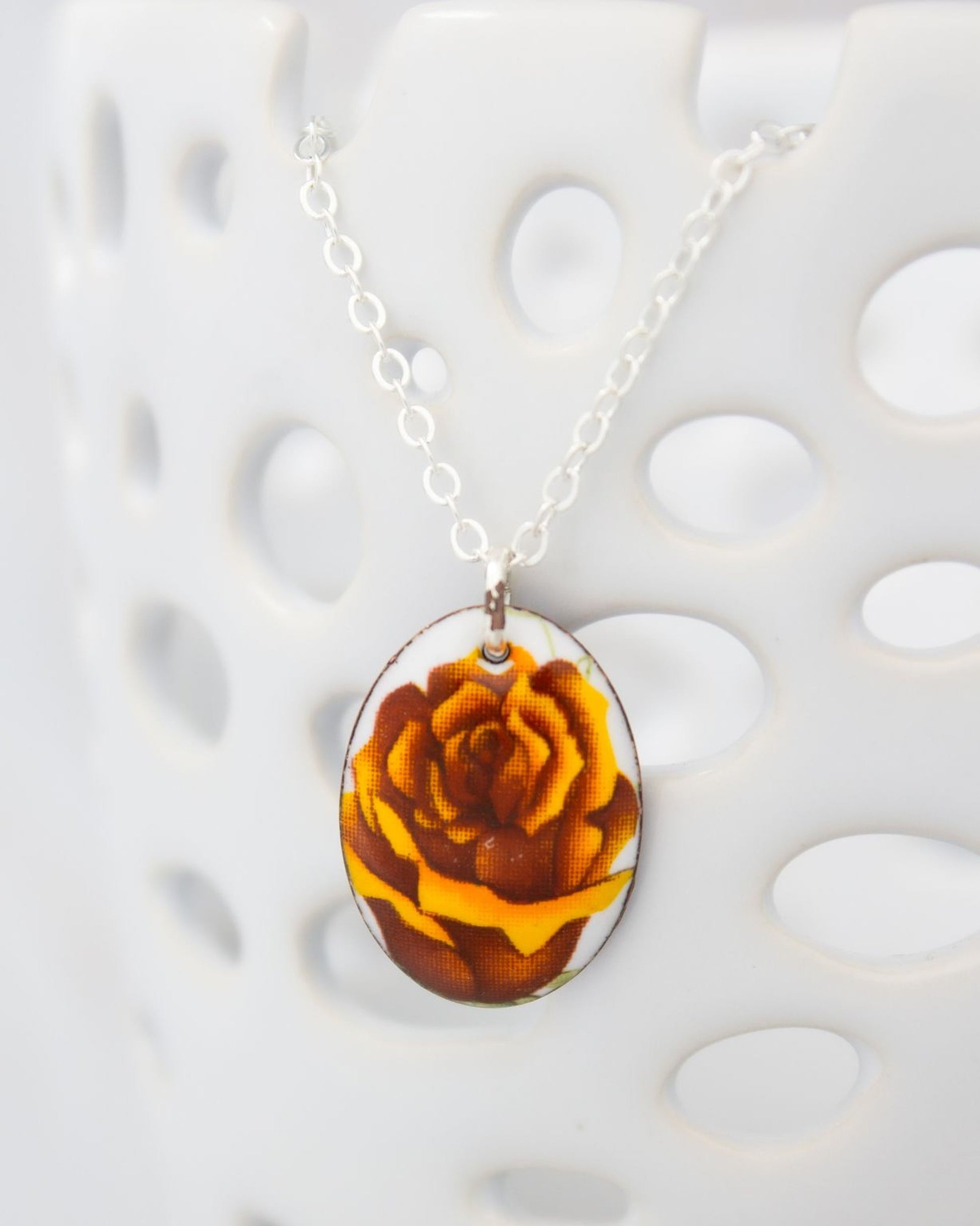 A necklace with a pendant featuring a close-up image of a flower, possibly a rose, in shades of brown and yellow.