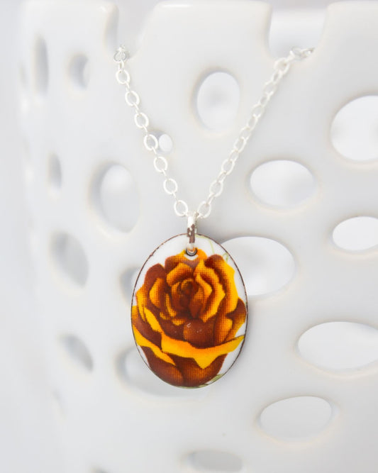A necklace with a pendant featuring a close-up image of a flower, possibly a rose, in shades of brown and yellow.