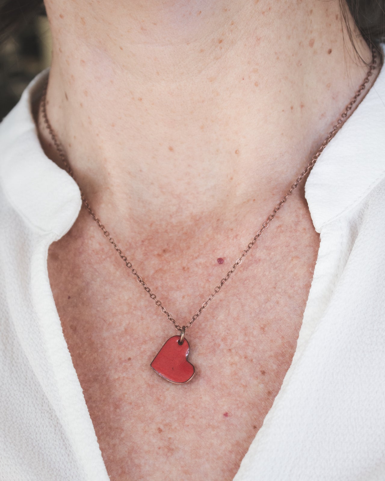A close-up view of a person's neck and chest area, featuring a red heart-shaped pendant necklace.