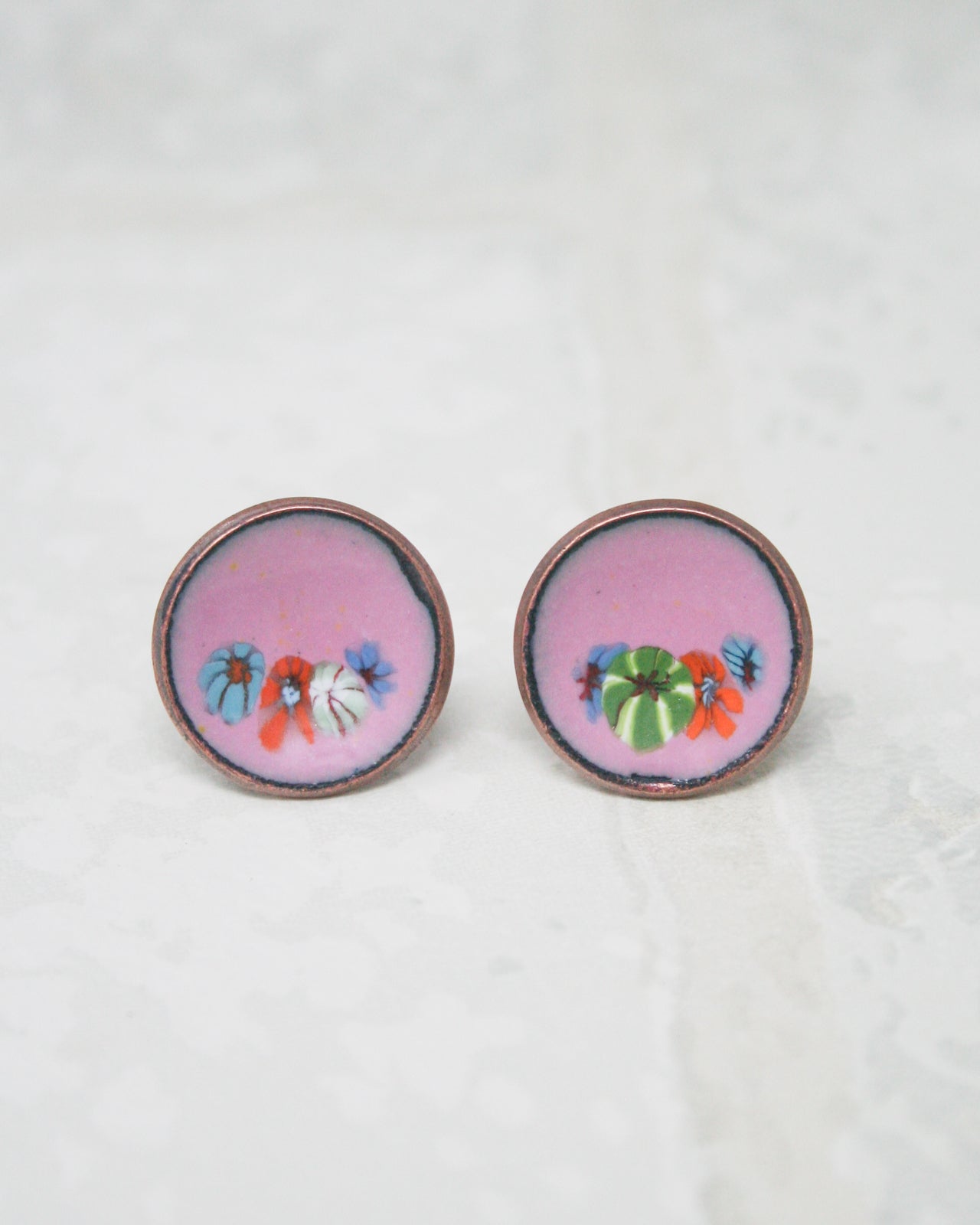 two round earrings with a floral design, placed on a white surface.