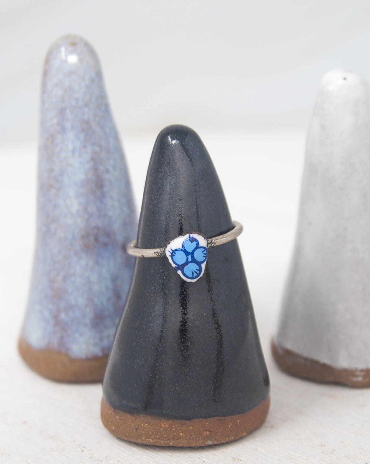 A black ceramic ring stand holding a silver ring with a blue flower design.