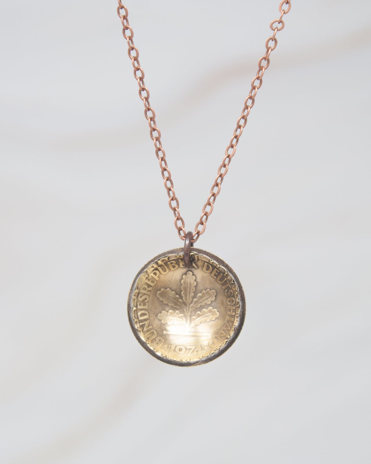 A necklace with a round pendant featuring a design of leaves and text.
