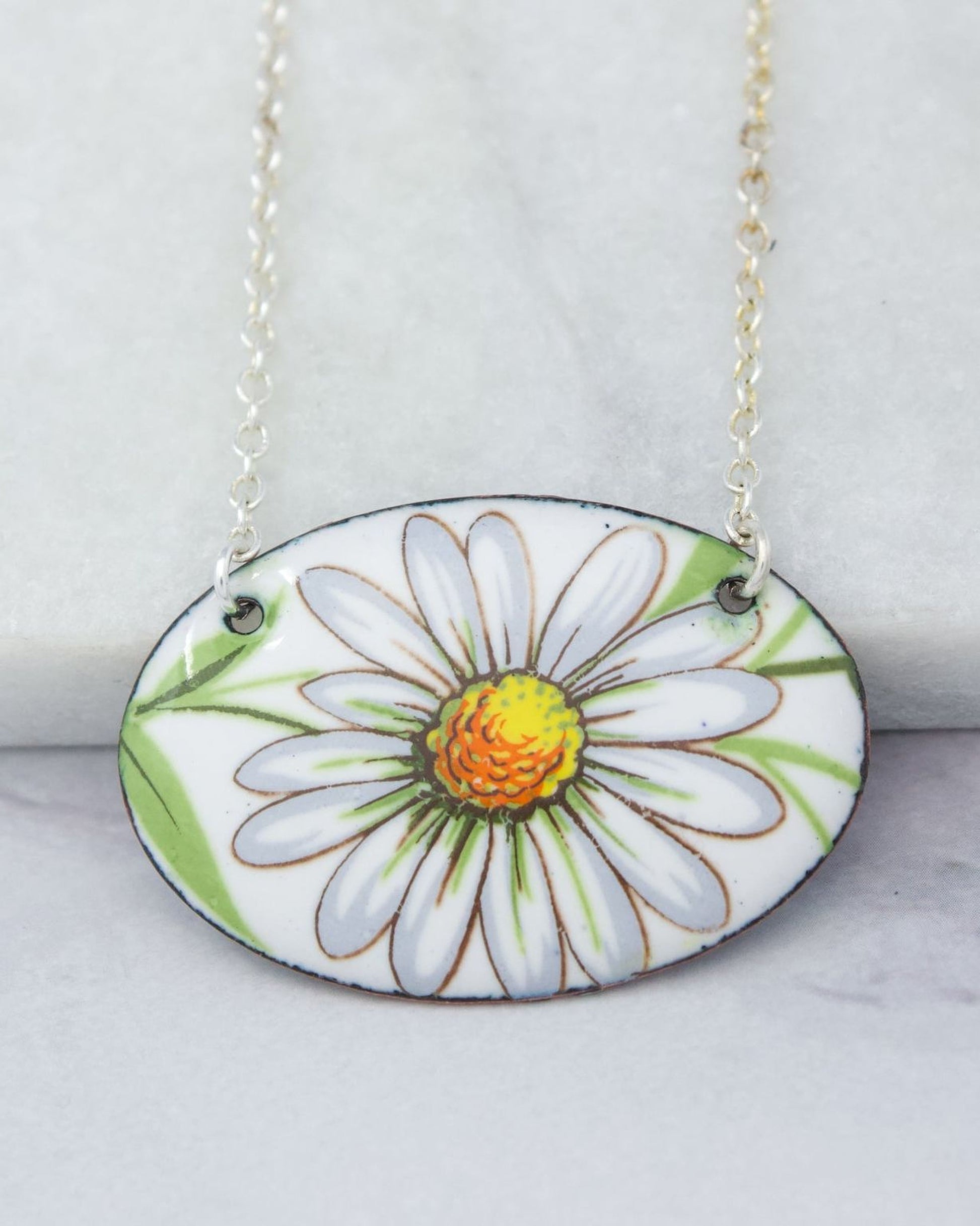 A necklace with a pendant featuring a white daisy flower design.
