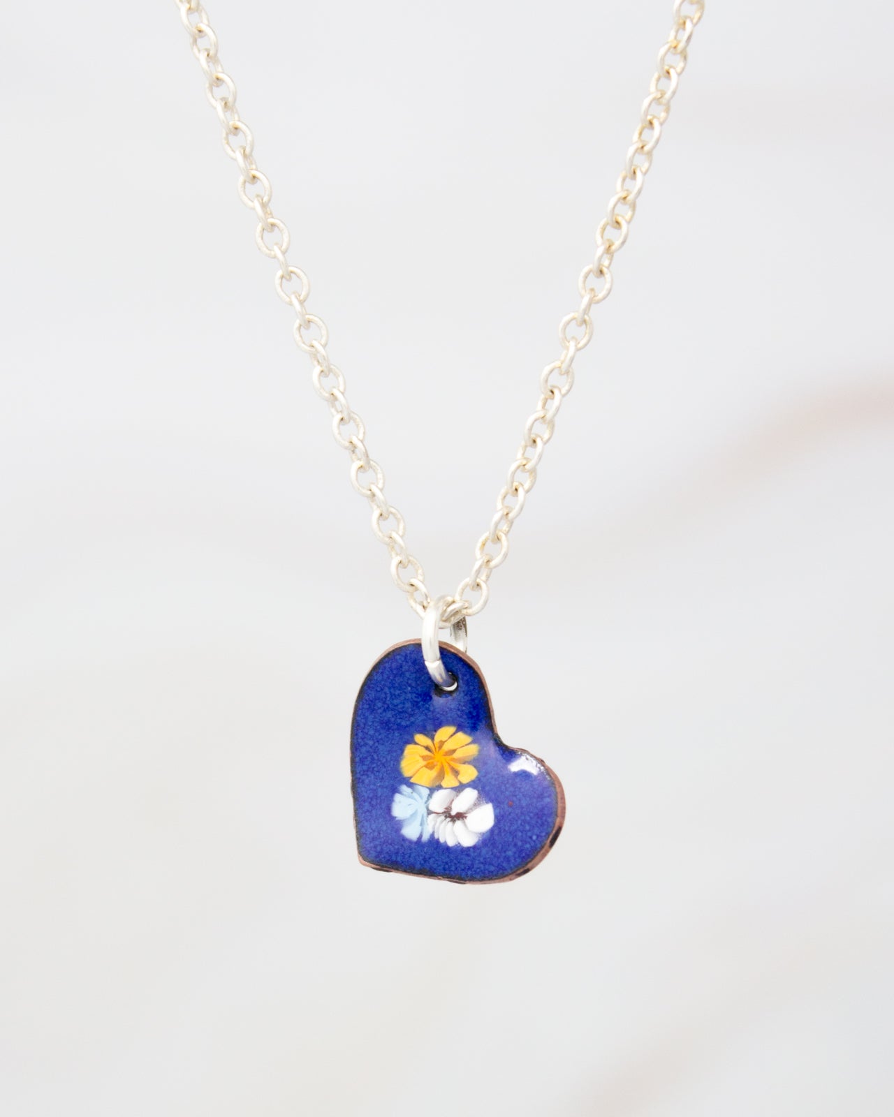 A delicate blue heart-shaped pendant with a floral design hangs from a silver chain.