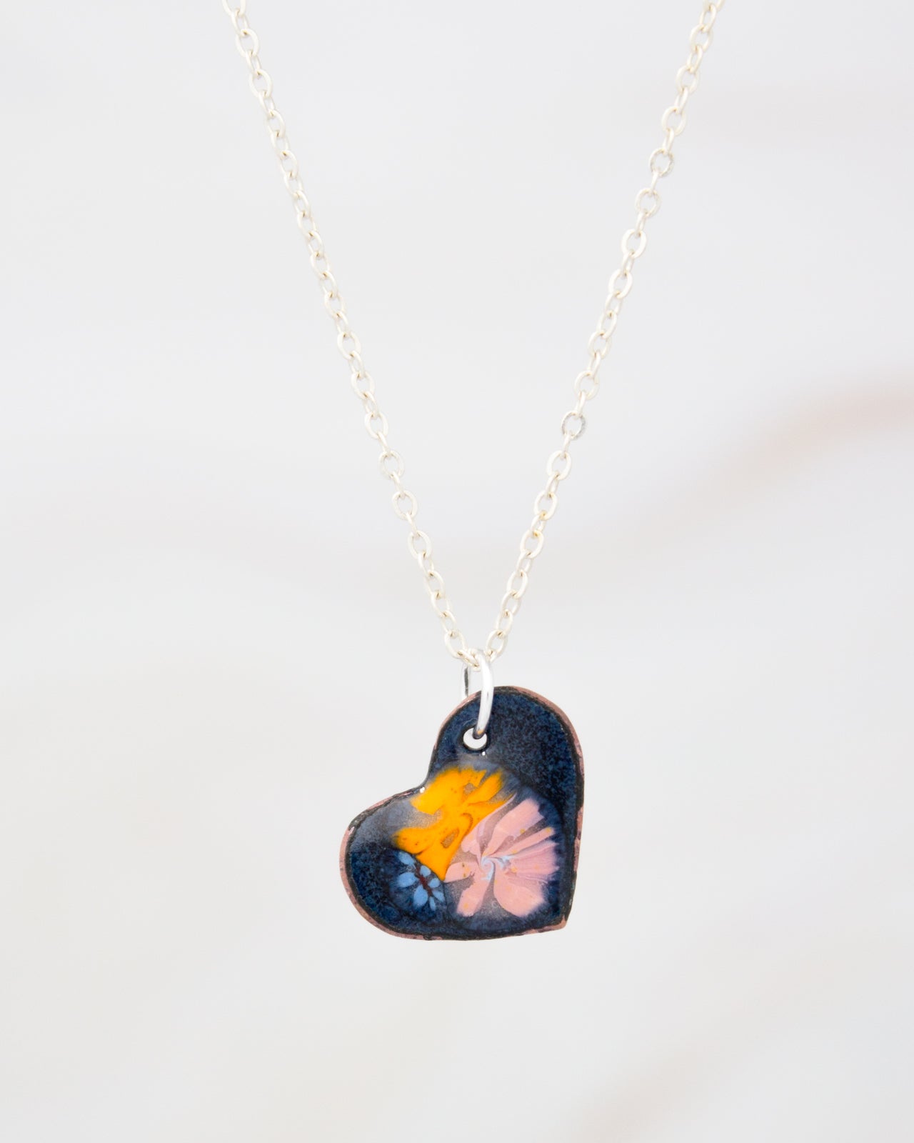 A heart-shaped pendant necklace with a floral design on a dark background.