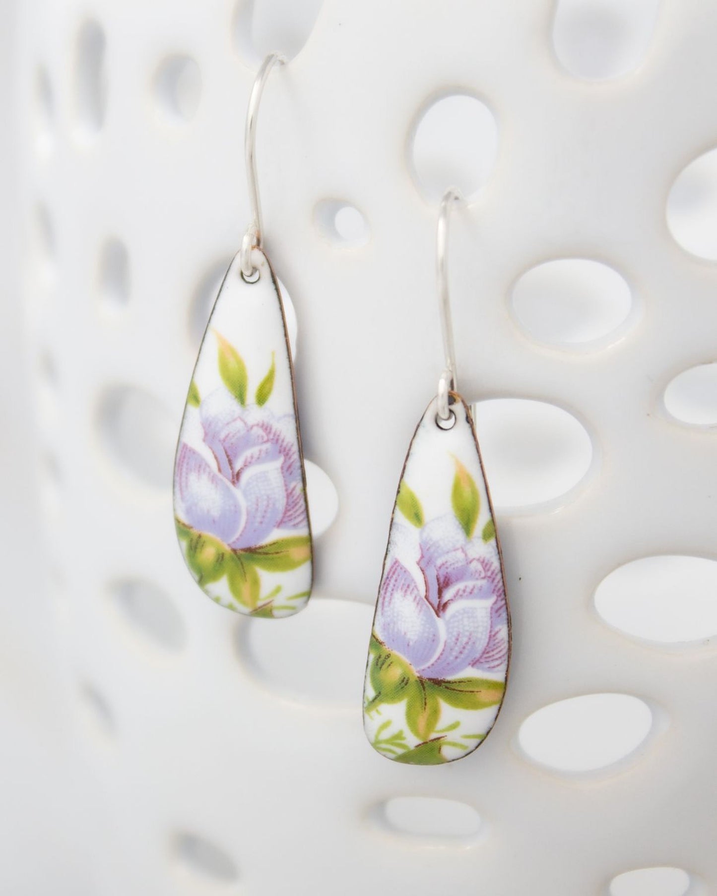 A pair of earrings with a floral design, featuring a purple flower and green leaves.