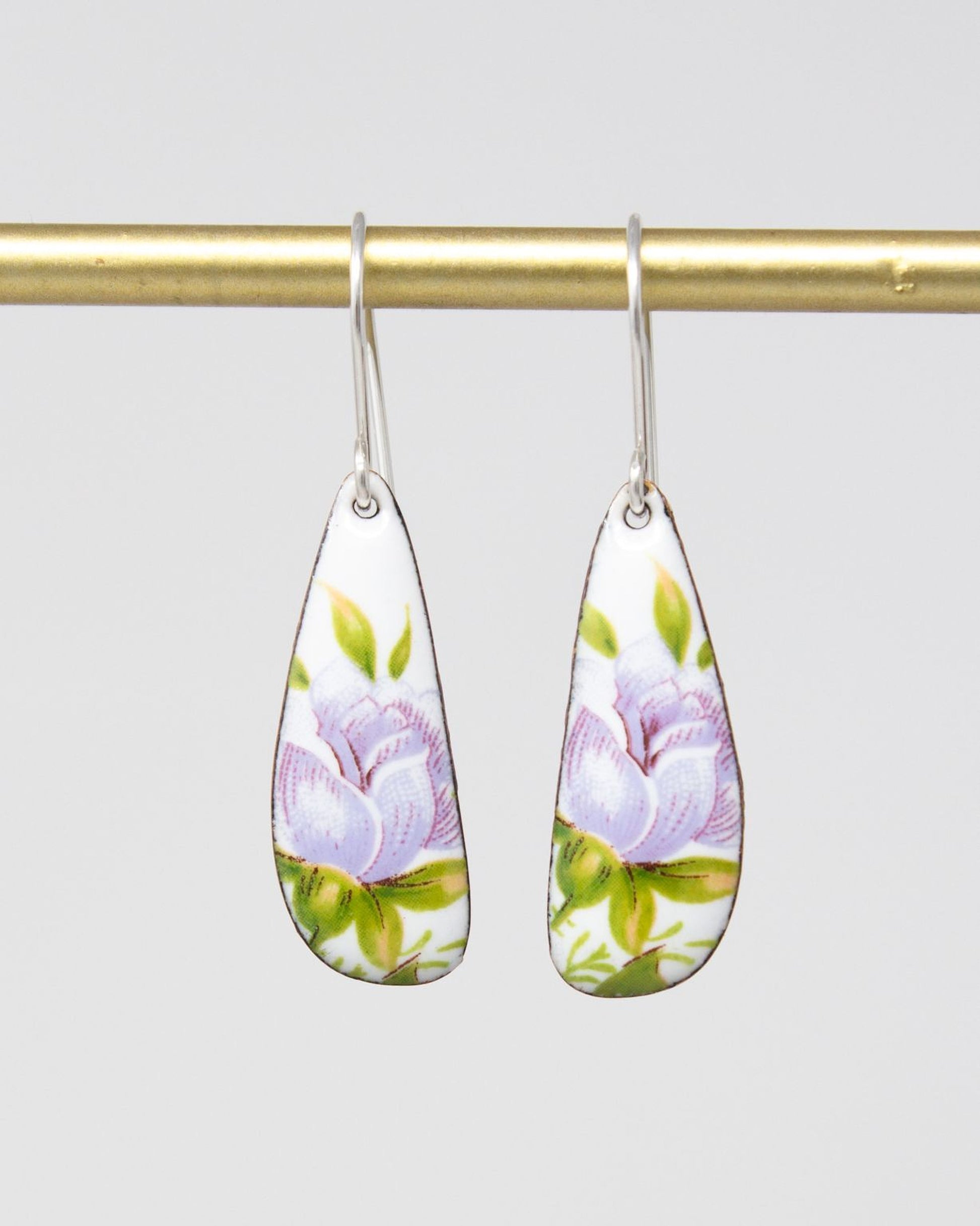 A pair of earrings with a floral design, featuring a white rose with green leaves and purple petals.