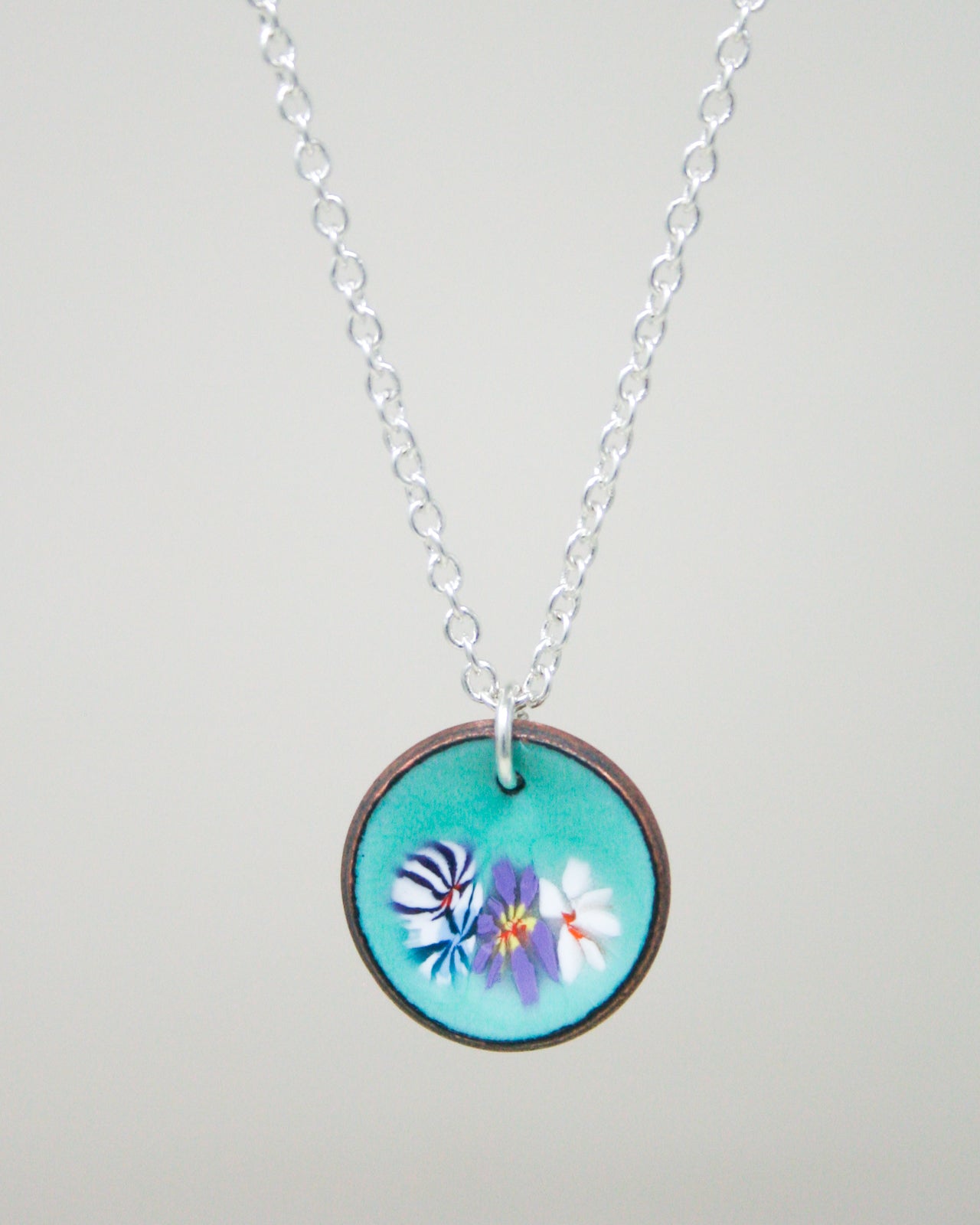 A necklace with a circular pendant featuring a floral design in turquoise and white colors.