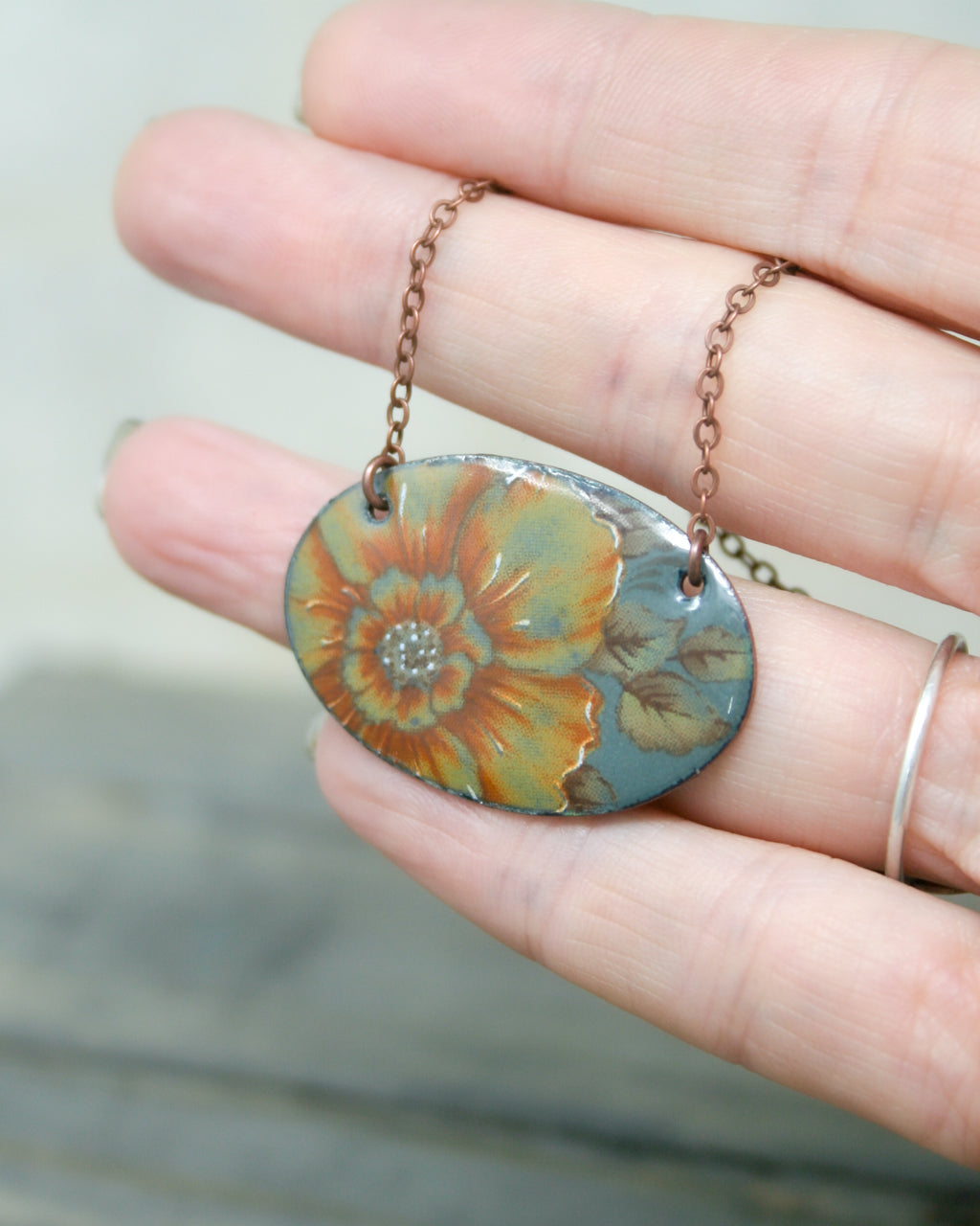 A hand holding a necklace with a pendant featuring a colorful floral design.