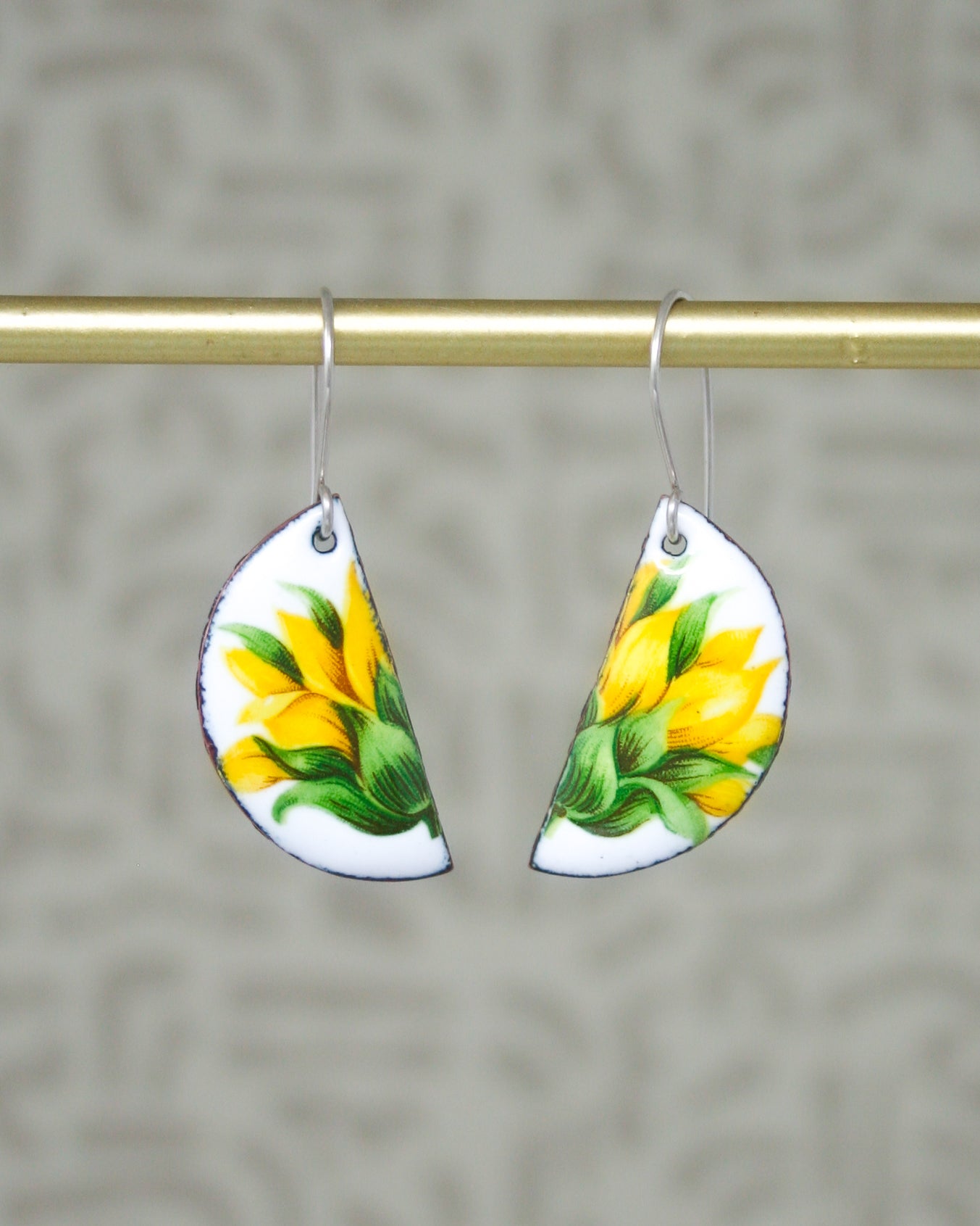 a pair of sunflower earrings hanging from a gold bar