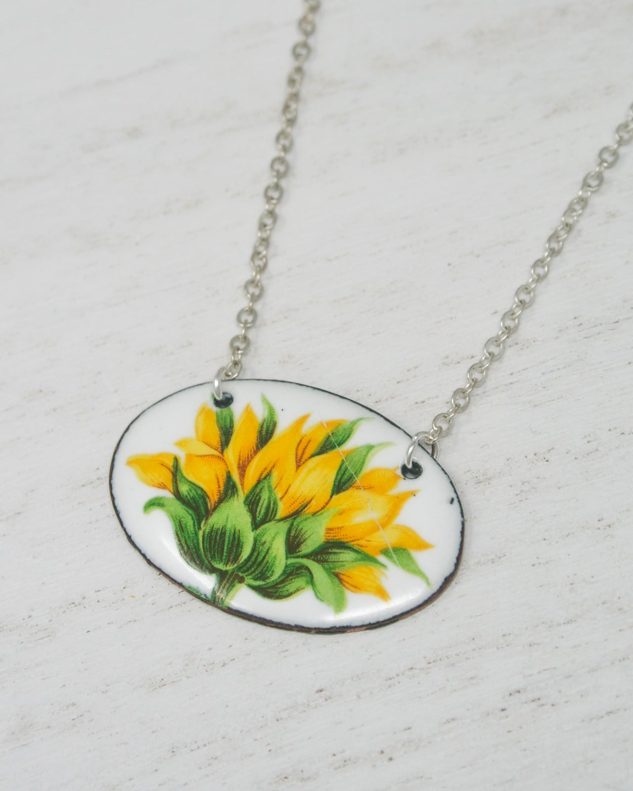 A necklace with a pendant featuring a close-up image of a yellow flower with green leaves.